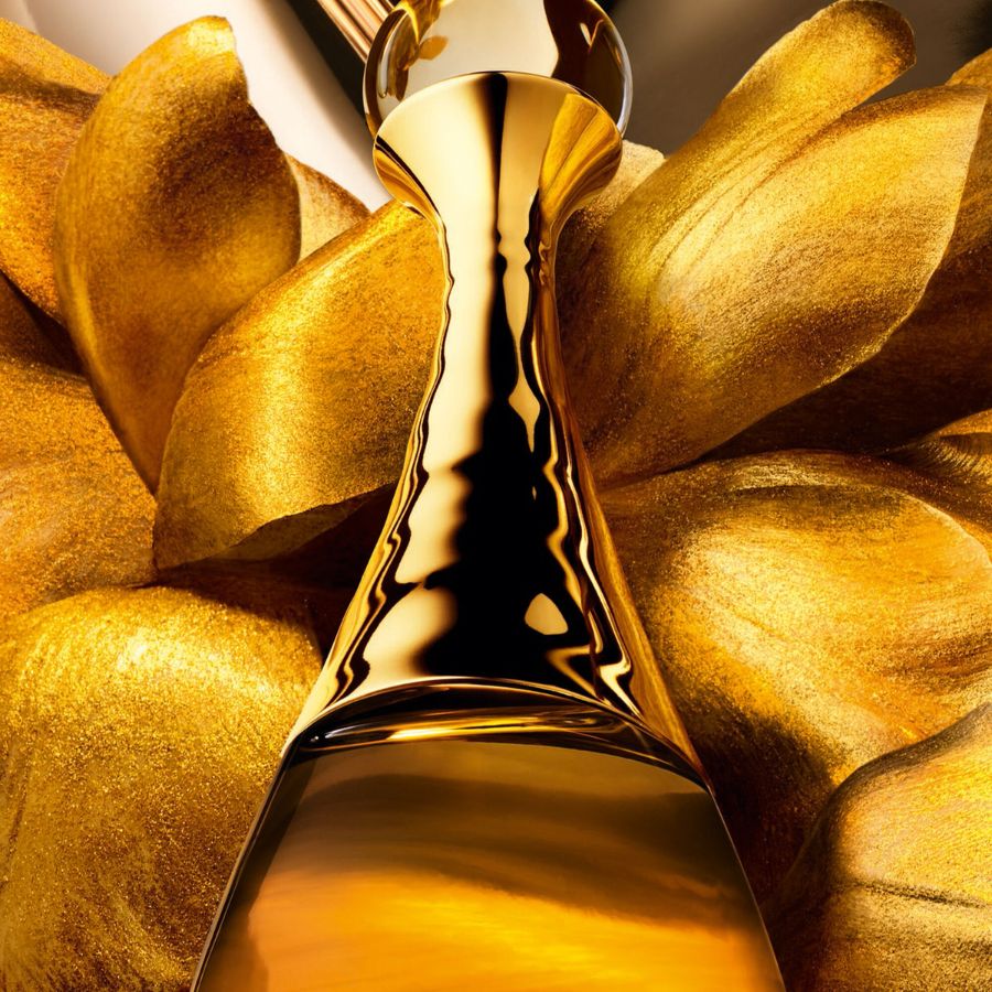 Arany virágok között egy arany színű, karcsú parfümös üveg látható, mely eleganciát és luxust sugároz.