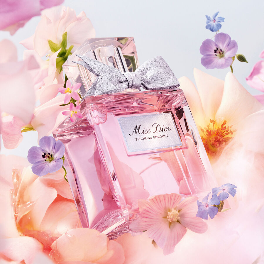 Ein rosafarbener Miss Dior Blooming Bouquet Duft, umgeben von zarten Blüten, verspricht einen blumigen und femininen Duft.