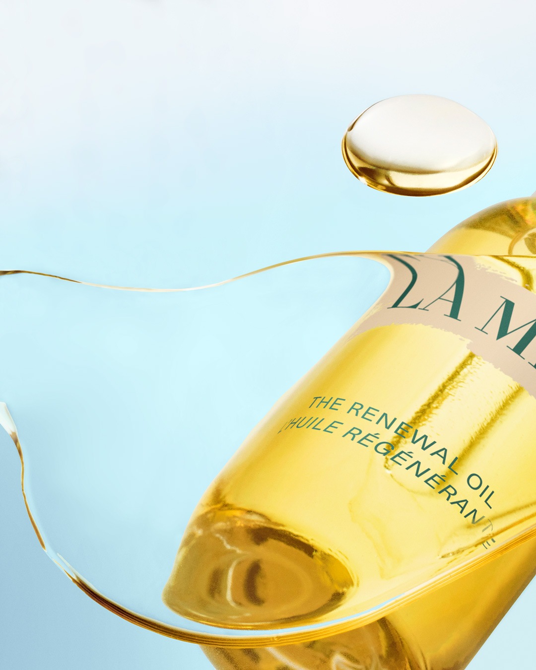 Gouden La Mer The Renewal Oil fles met een druppel olie op een lichtblauwe achtergrond.