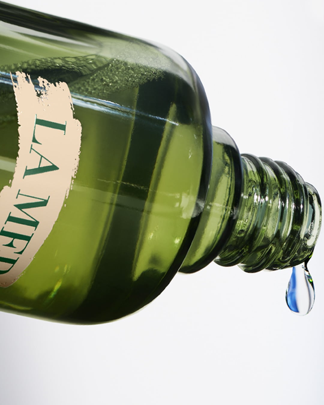 Close-up van een groene La Mer fles met een druppel vloeistof die eraf valt, wat de essentie van hydratatie en luxe weergeeft.