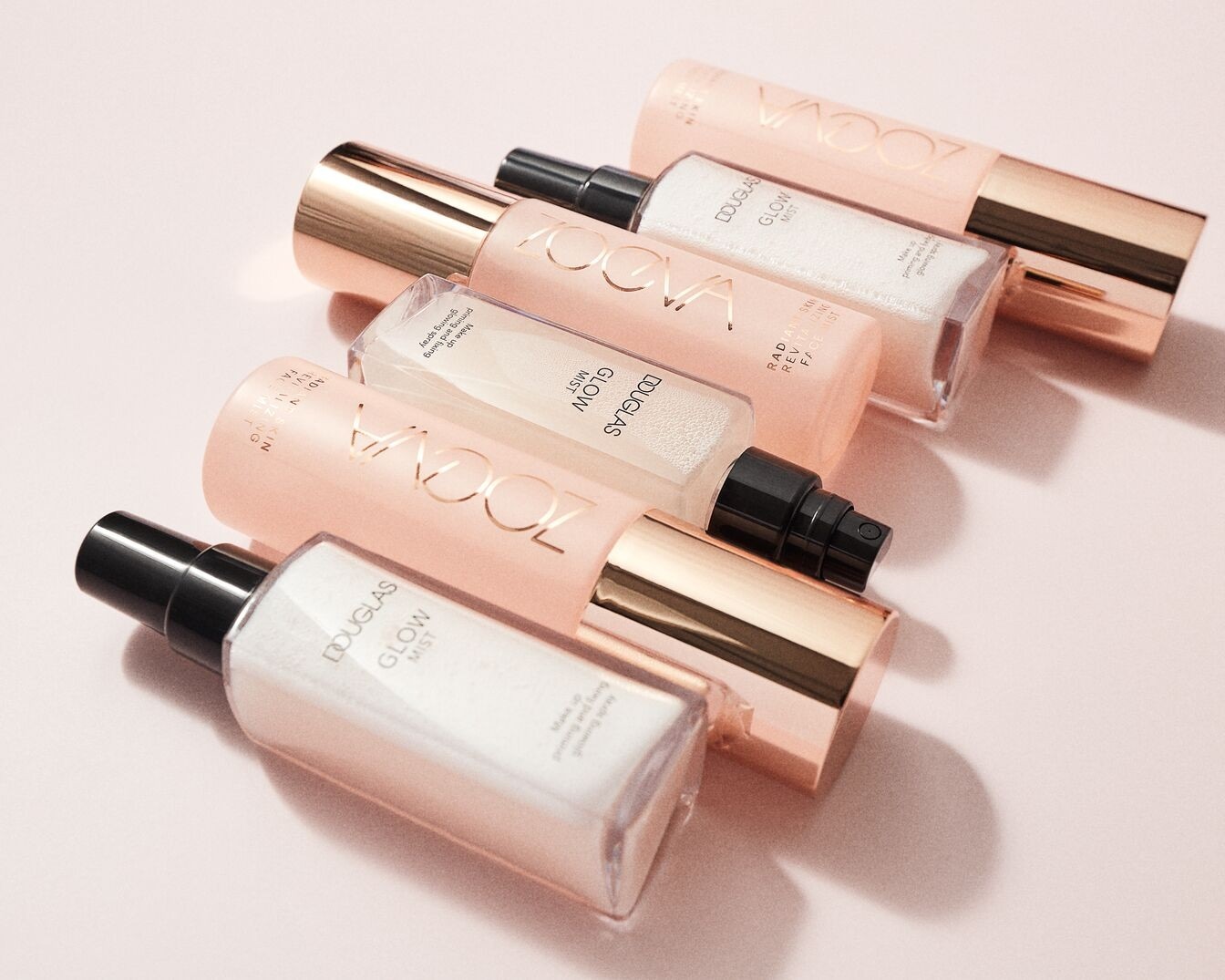 Nahaufnahme von Douglas Glow Mist und Zoeva Radiant Skin Revitalizing Face Mist in rosa Verpackung mit goldenen Akzenten, die Make-up-Grundierung und Fixierspray versprechen.