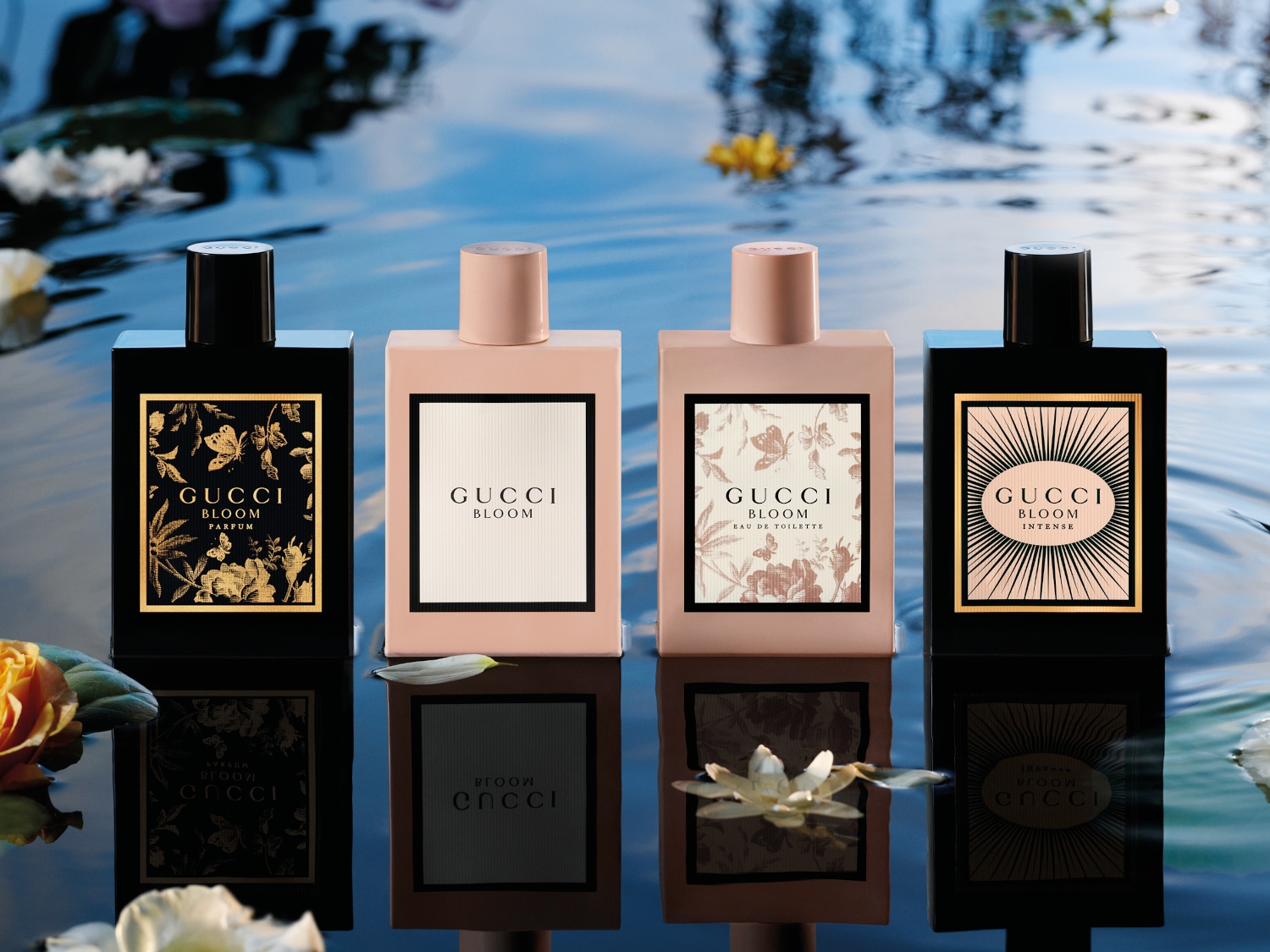 Dwa flakony perfum Gucci Bloom Intense i Gucci Bloom otoczone kwiatami w odcieniach bieli i fioletu, zanurzone w wodzie, tworzące subtelną i elegancką kompozycję.