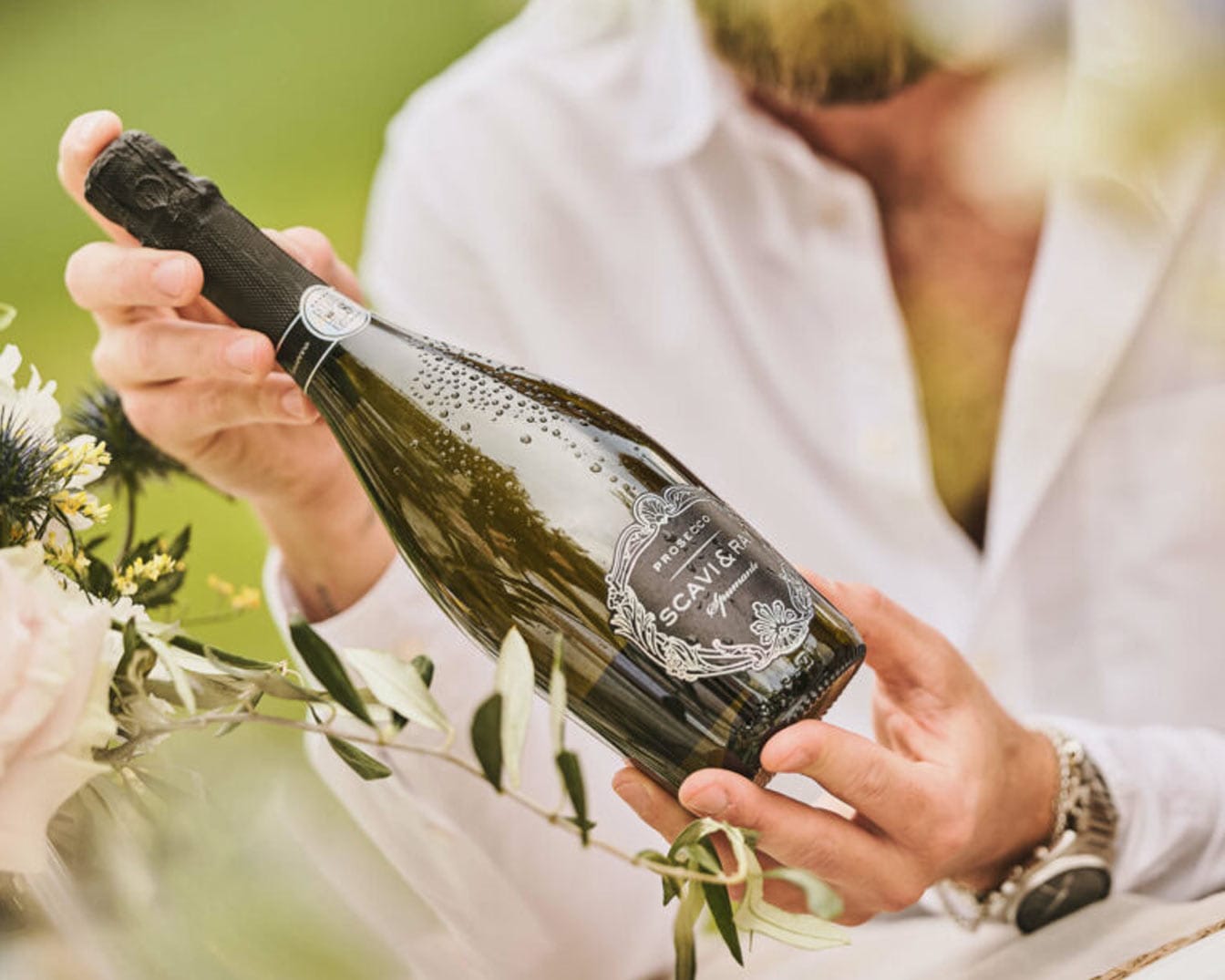 Ein Mann im weißen Hemd hält eine grüne Flasche Scavi & Ray Prosecco Spumante mit Wassertropfen in den Händen.