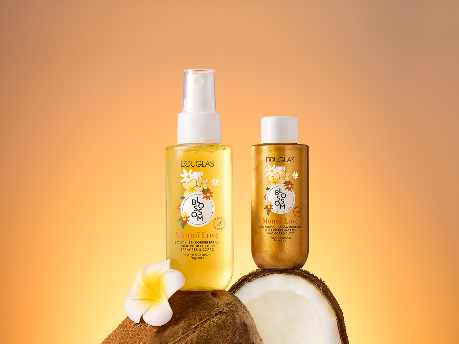 Twee Douglas Blossom Monoi Love producten: een gele bodymist en een gouden glow body oil, beide met een bloemmotief, op een kokosnoot met een witte bloem.