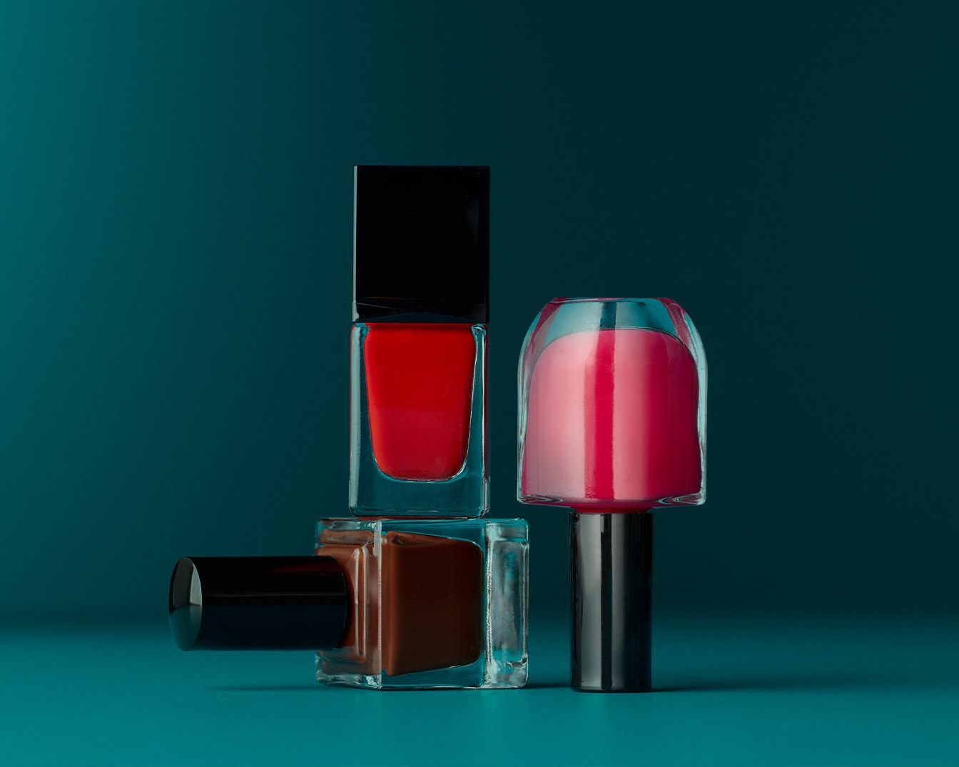 Découvrez un assortiment de vernis à ongles : un rouge vibrant, un rose délicat et un brun riche, présentés dans des flacons élégants sur un fond turquoise.