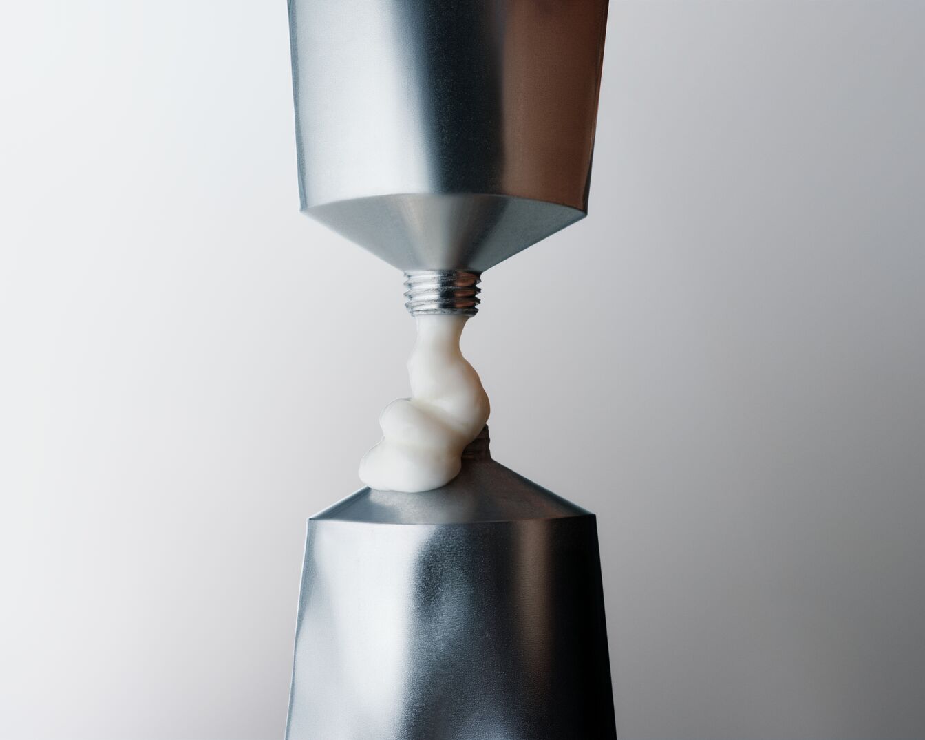 Deux tubes argentés pressent une crème blanche épaisse, illustrant l'union et la transformation des soins de la peau.