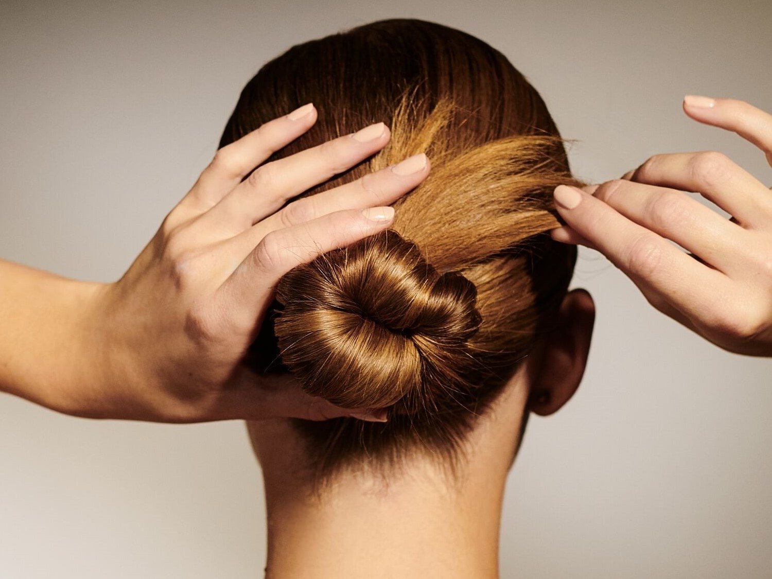 Nahaufnahme von braunem Haar, das zu einem Knoten geformt wird, wobei die Hände das Haar an Ort und Stelle halten.