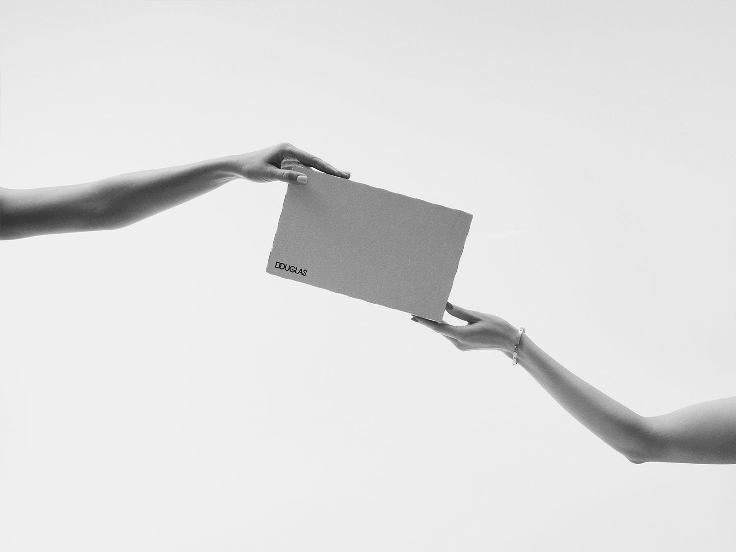 Deux mains se tendent un paquet Douglas sur un fond blanc épuré, évoquant l'échange et le partage de produits de beauté.