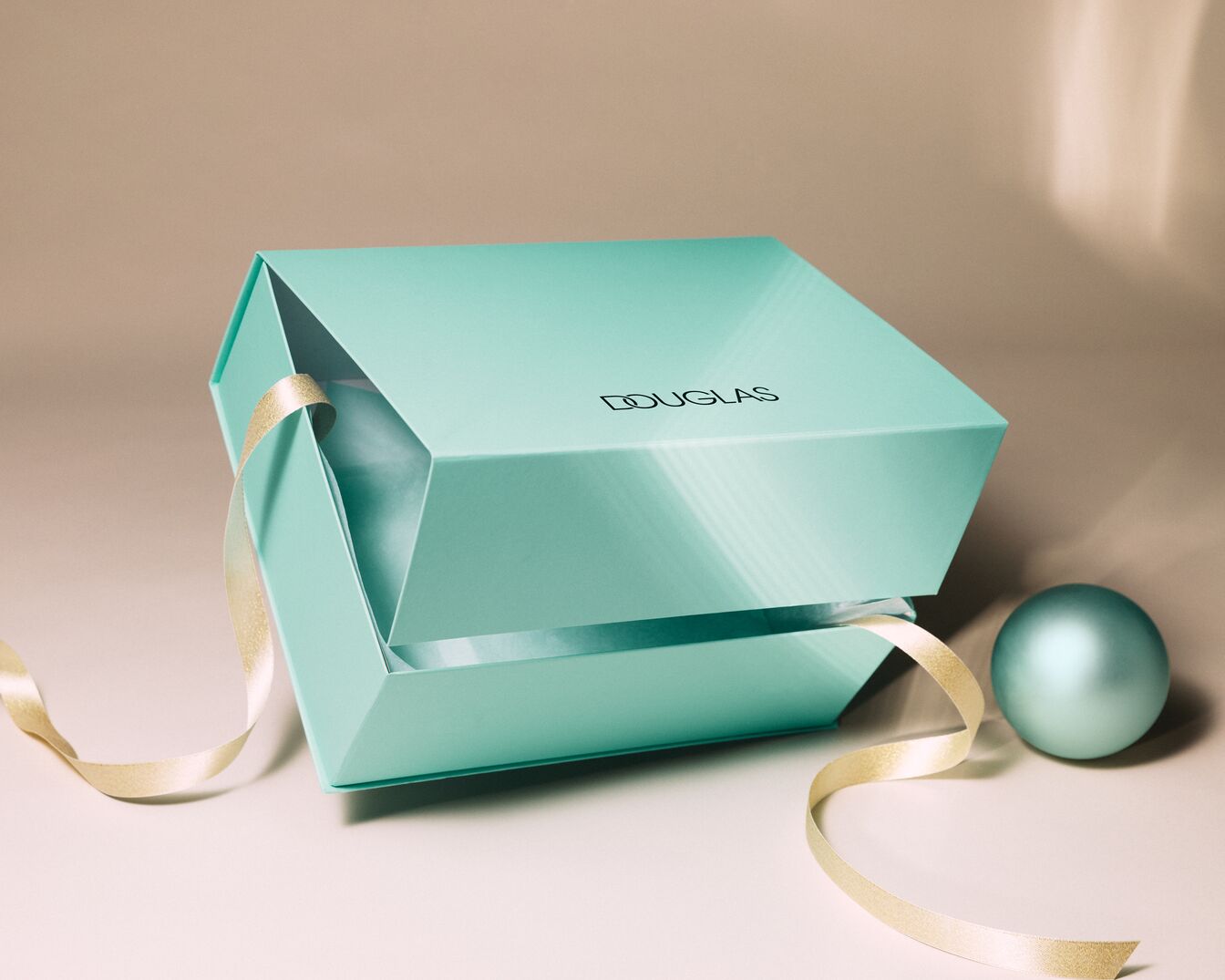 Boîte turquoise ouverte de Douglas, ornée d'un ruban doré et d'une boule décorative assortie, évoquant l'élégance et le raffinement.
