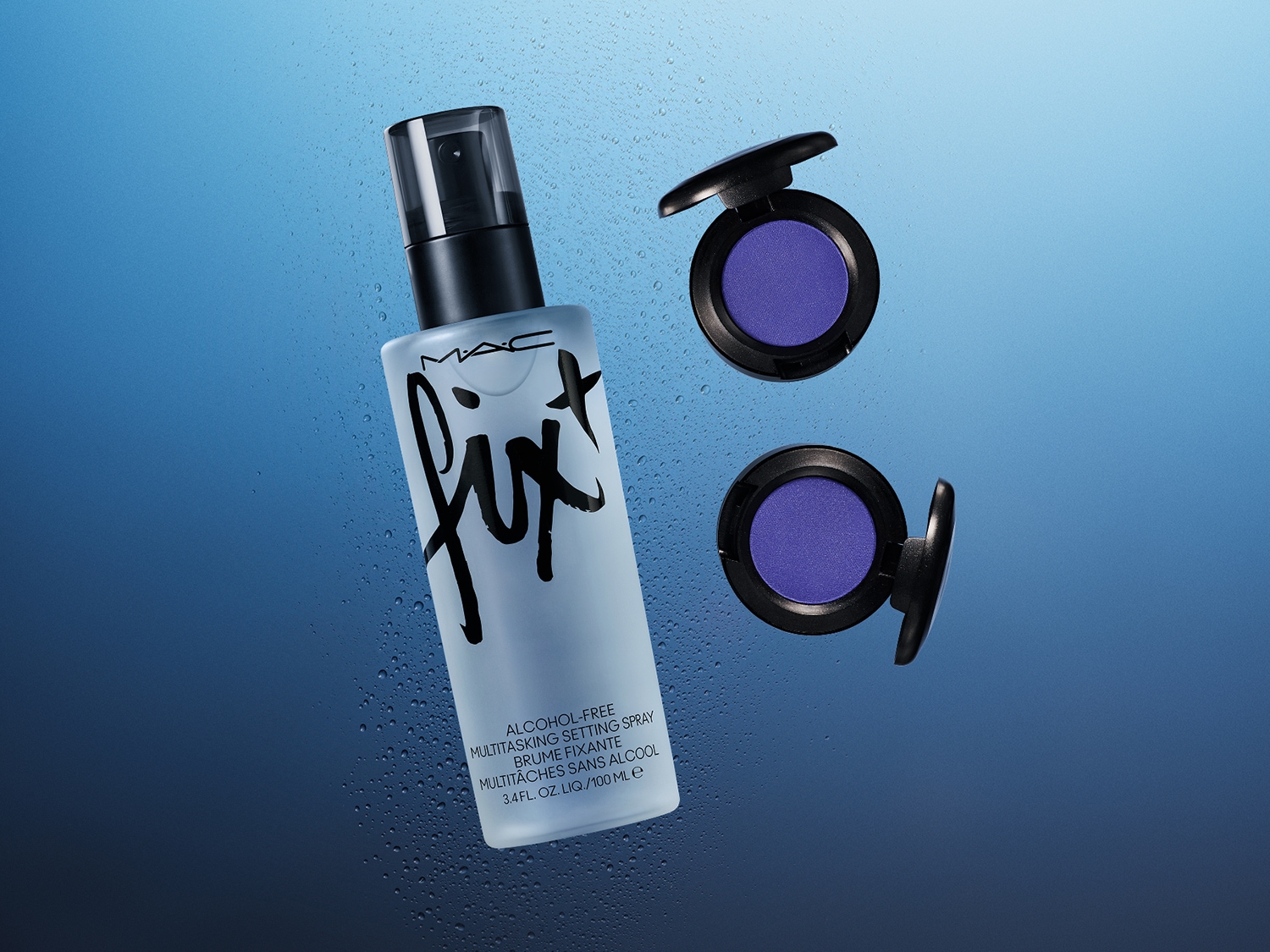Een alcoholvrije MAC Fix+ setting spray in een heldere fles met zwarte accenten, samen met twee paarse oogschaduws in zwarte doosjes.