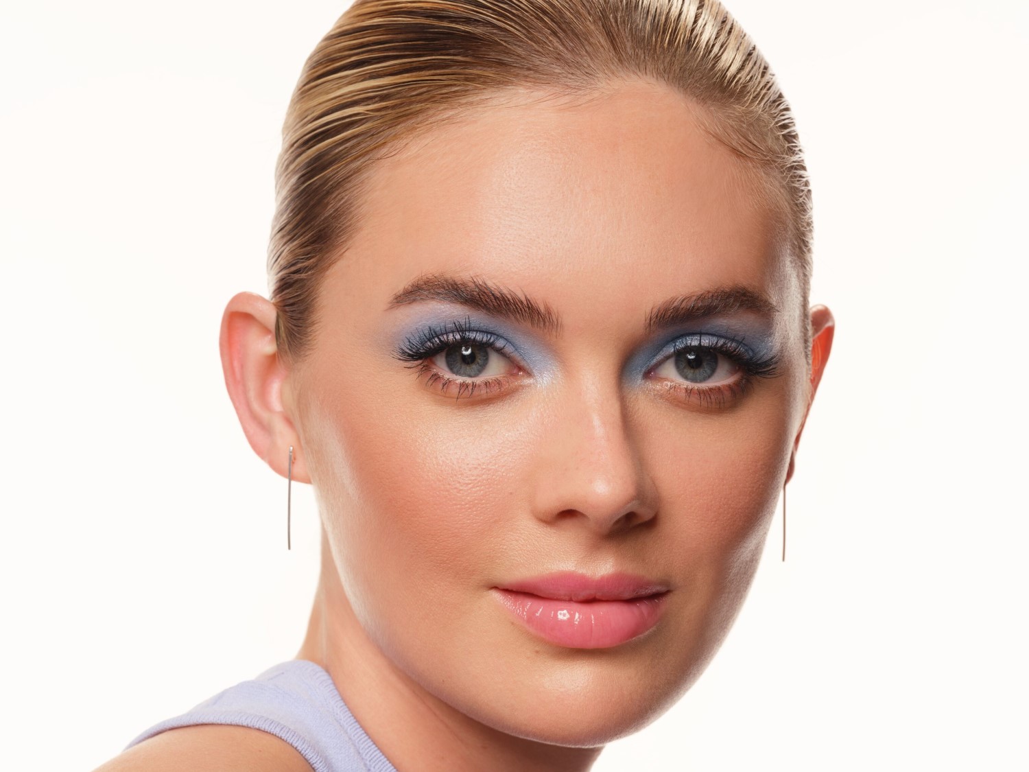 Nahaufnahme eines blonden Models mit blauem Lidschatten, rosigen Wangen und glänzenden Lippen, das einen frischen und strahlenden Look präsentiert.