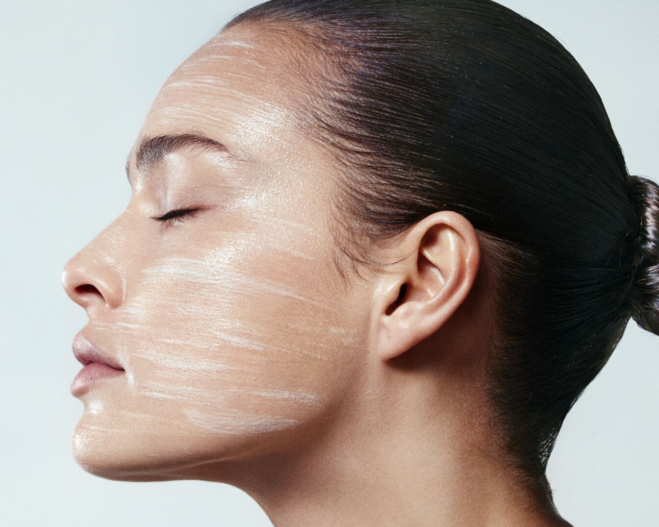 Egy nő profilból látható, arcán fehér krémcsíkokkal, szeme csukva, haja kontyba fogva.