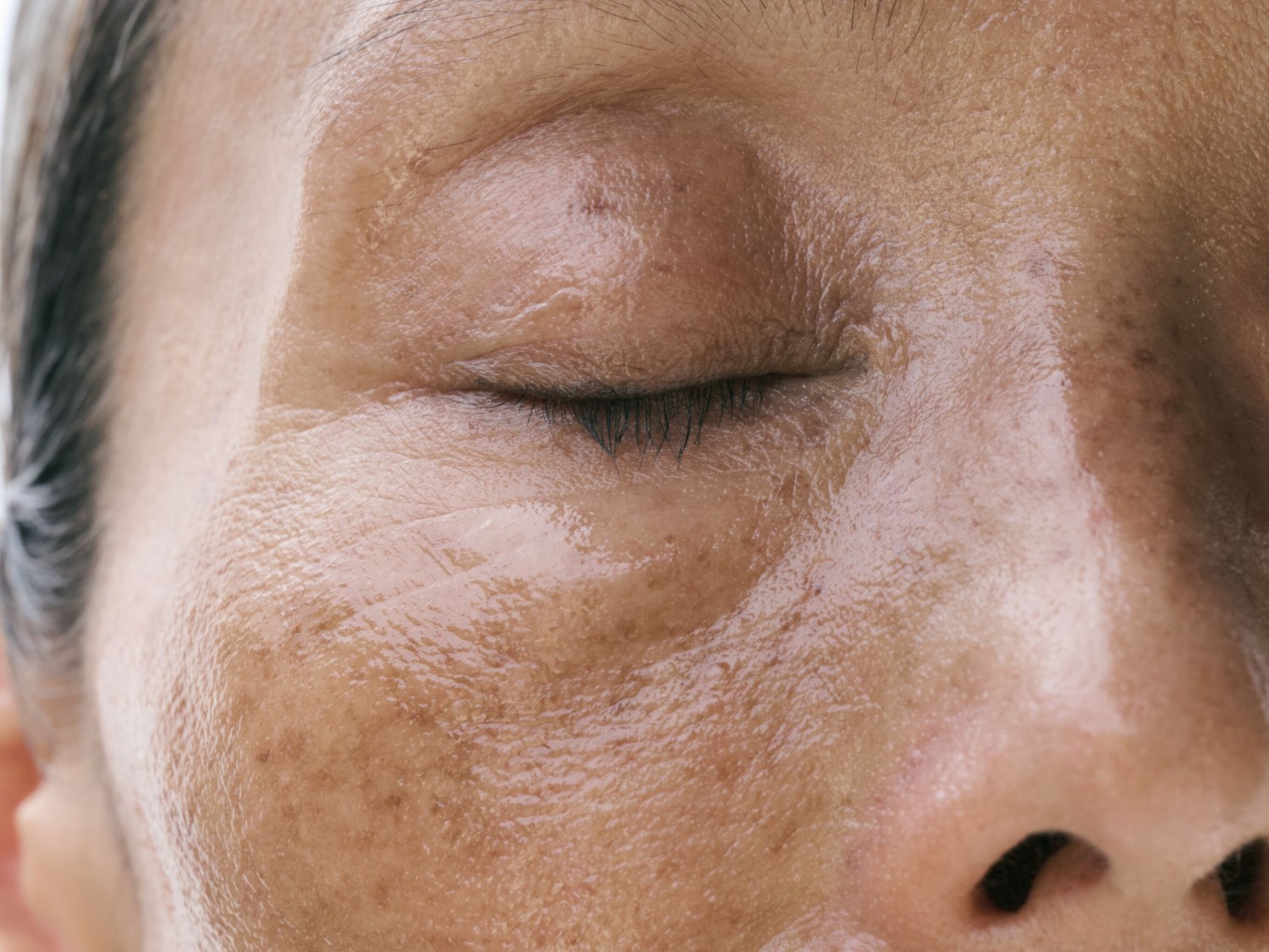 Gedetailleerd close-up van een gezicht met een gesloten oog, waarbij de huidtextuur en kleine imperfecties zoals sproeten en fijne lijntjes rond het oog te zien zijn.