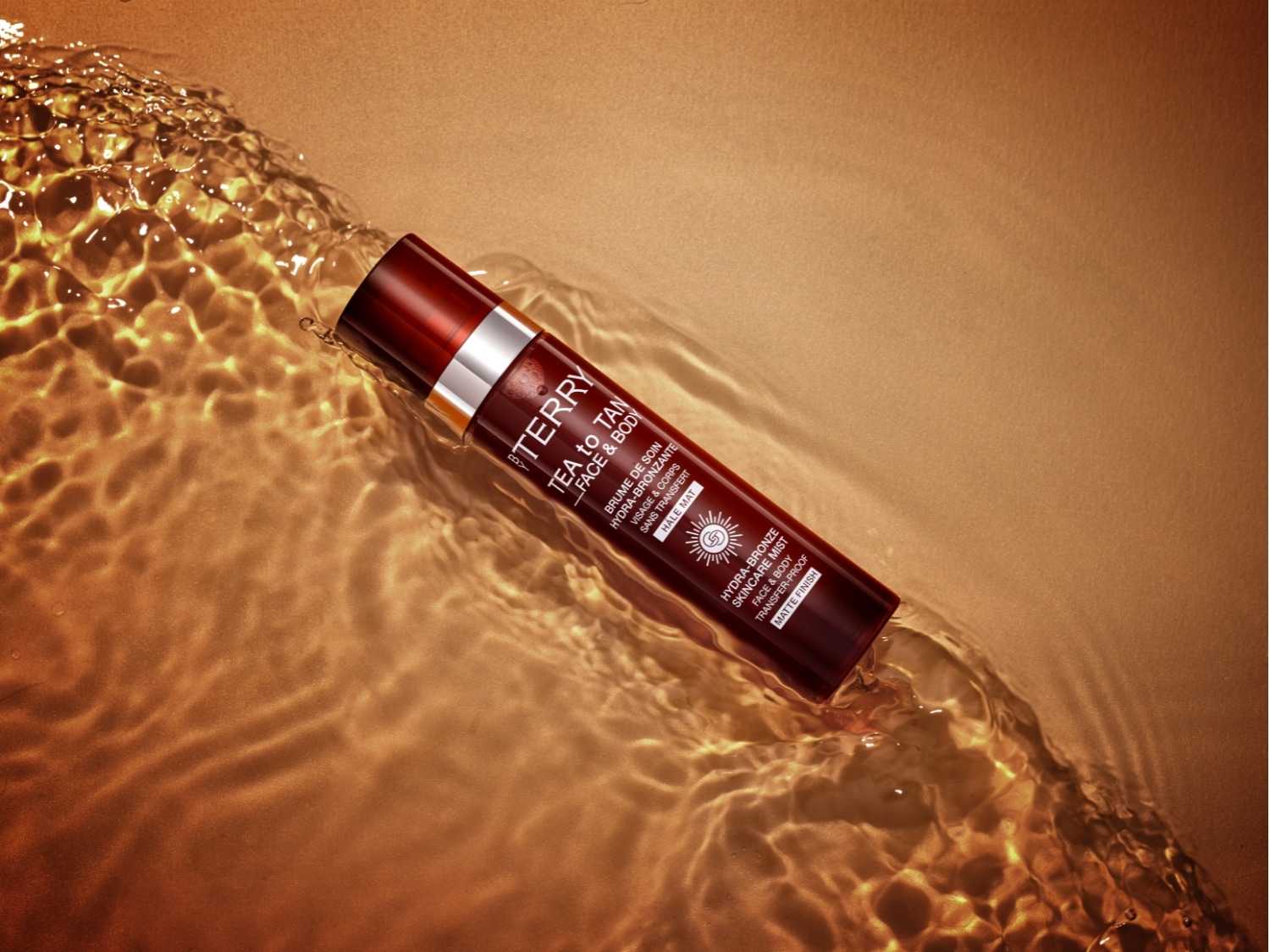 Brązująca mgiełka do twarzy i ciała By Terry Tea to Tan w brązowym opakowaniu zanurzona w wodzie, zapewniająca efekt matowego wykończenia i naturalnej opalenizny.