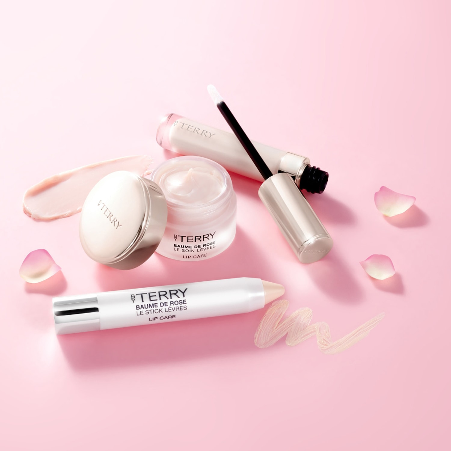 Kolekcja do pielęgnacji ust By Terry Baume De Rose na różowym tle, w tym balsam w słoiczku, sztyfcie i błyszczyk, zapewniające kompleksową pielęgnację i nawilżenie.