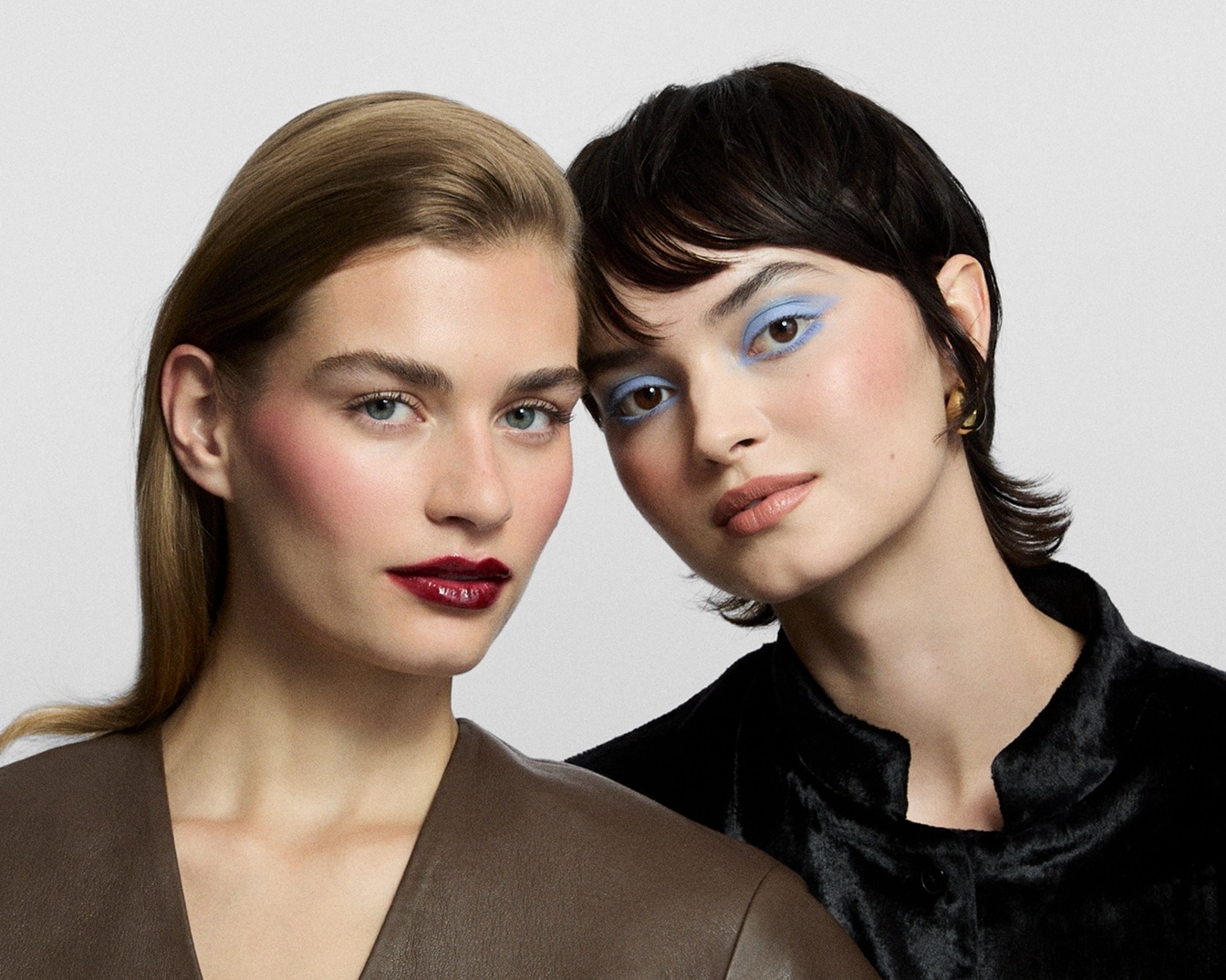 Zwei Models mit Make-up: Eine mit braunem Oberteil, rotem Lippenstift und Rouge, die andere mit schwarzem Oberteil und blauem Lidschatten.