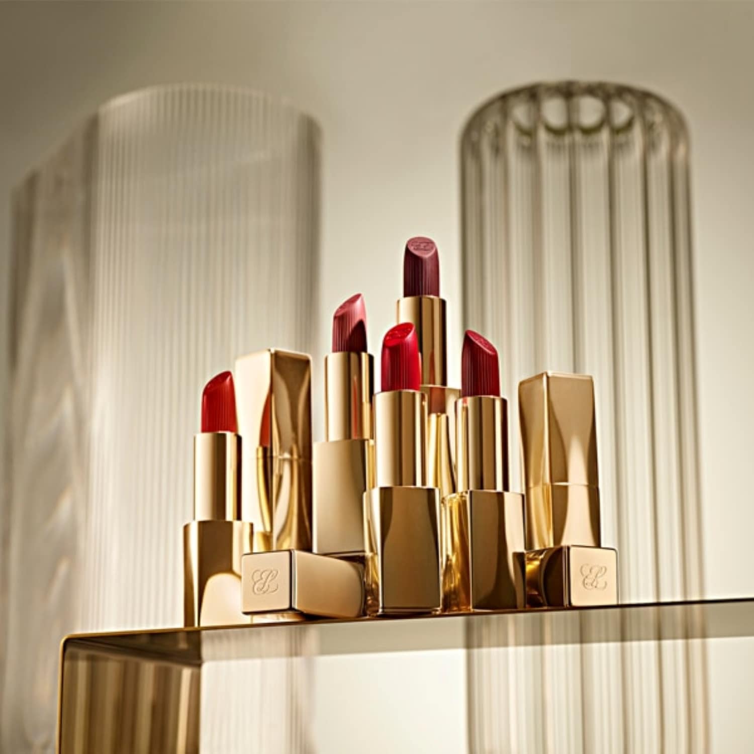 Eine Sammlung von goldenen Lippenstiften in verschiedenen Rot- und Lilatönen, die auf einer goldenen Oberfläche präsentiert werden.