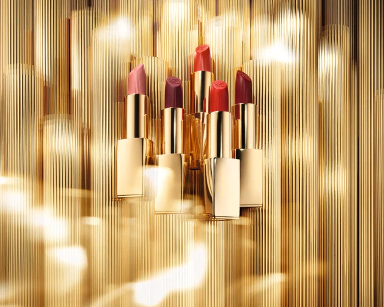 Eine Kollektion von Lippenstiften in verschiedenen Rot- und Rosatönen mit goldfarbenen Hülsen vor einem goldenen Hintergrund.