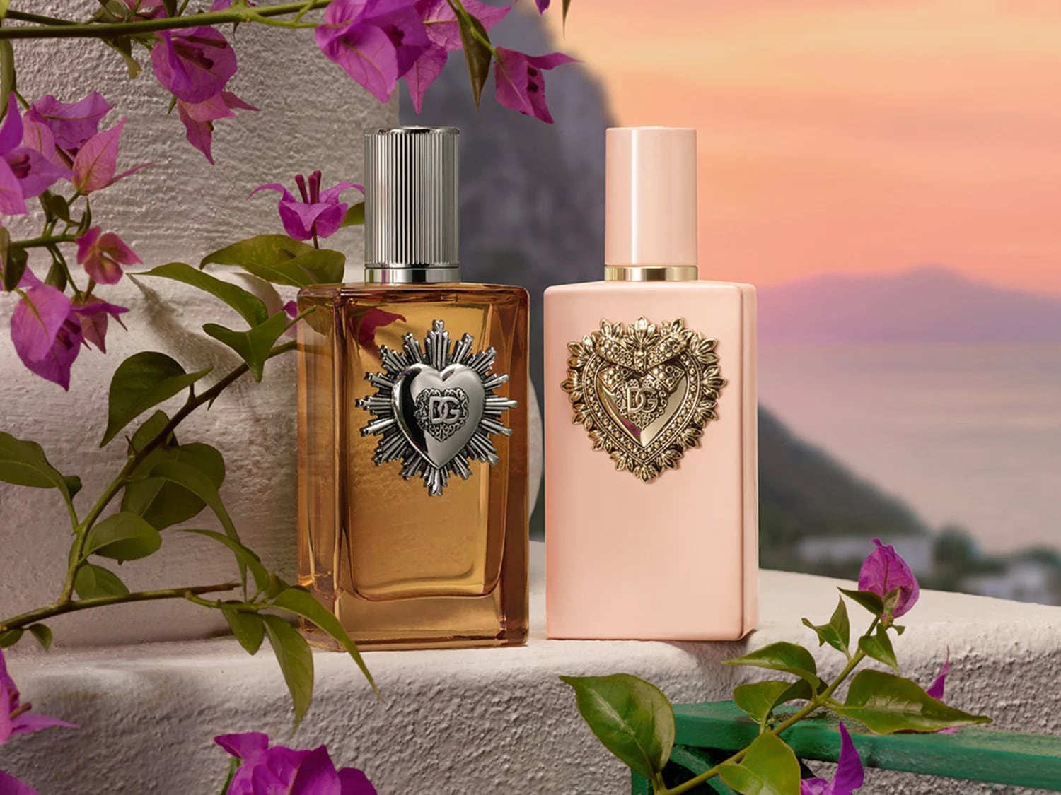 Twee Dolce & Gabbana Devotion geuren, de ene amberkleurig met een zilveren hart, de andere zachtroze met een gouden hart, beide versierd met bloemen.