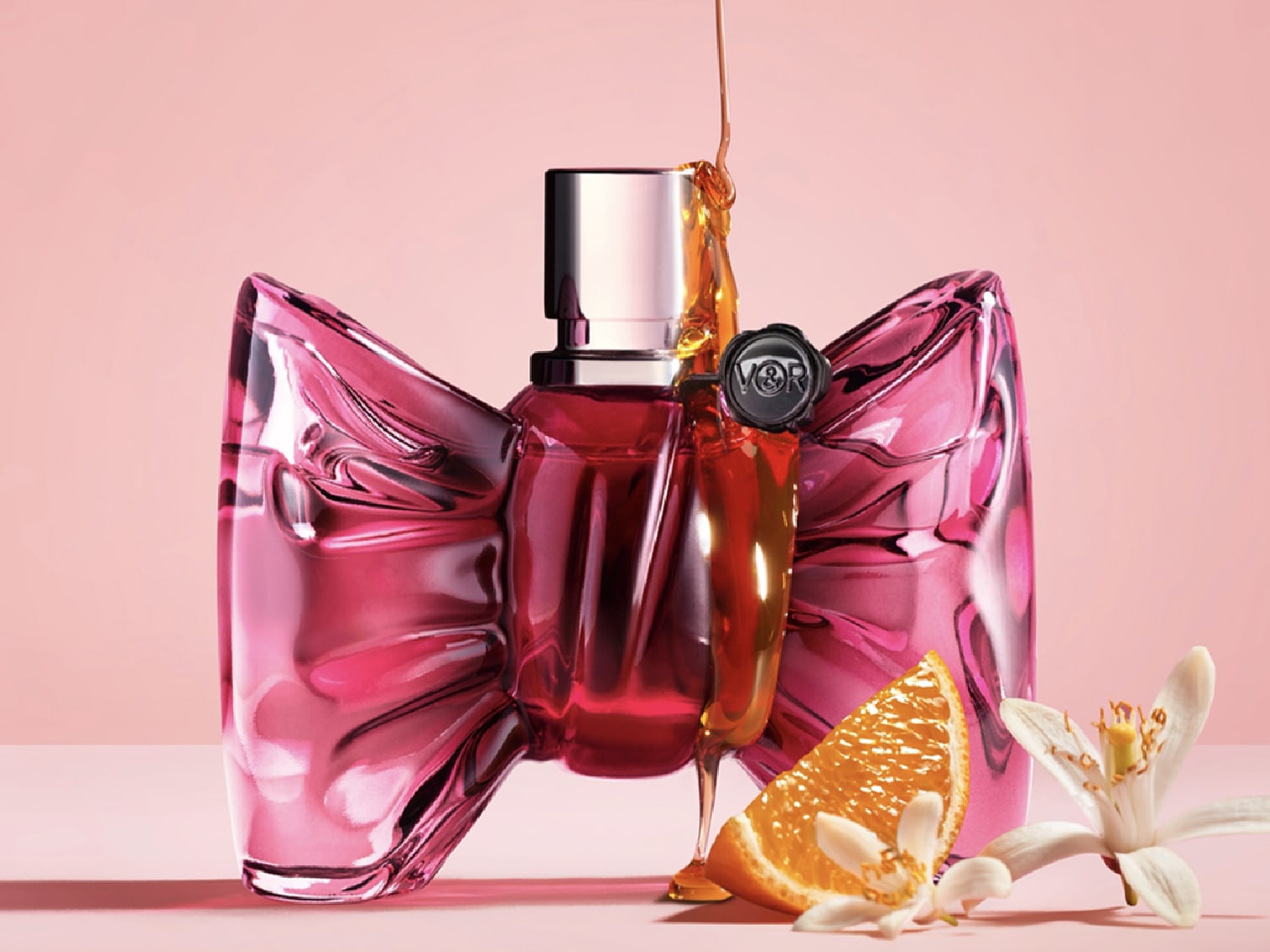 Découvrez le parfum dans un flacon rose en forme de nœud, rehaussé d'une touche d'orange et d'une coulée de miel dorée.