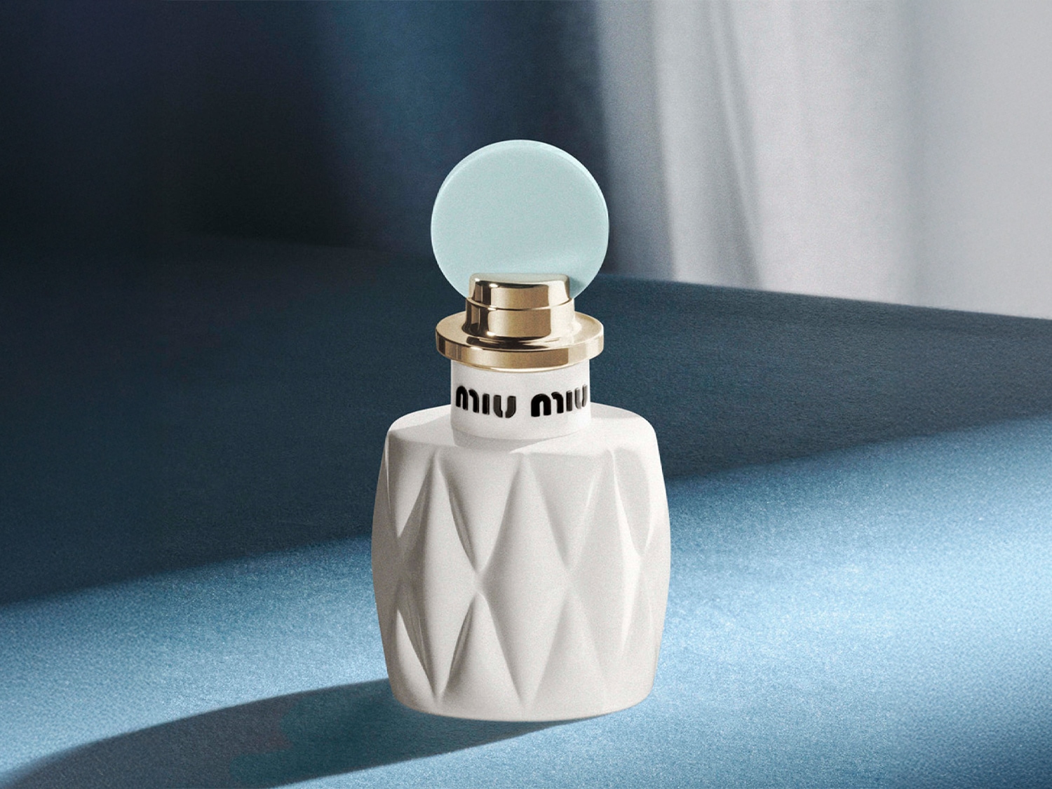Le flacon de parfum Miu Miu présente un design géométrique blanc avec un bouchon bleu clair et des accents dorés.