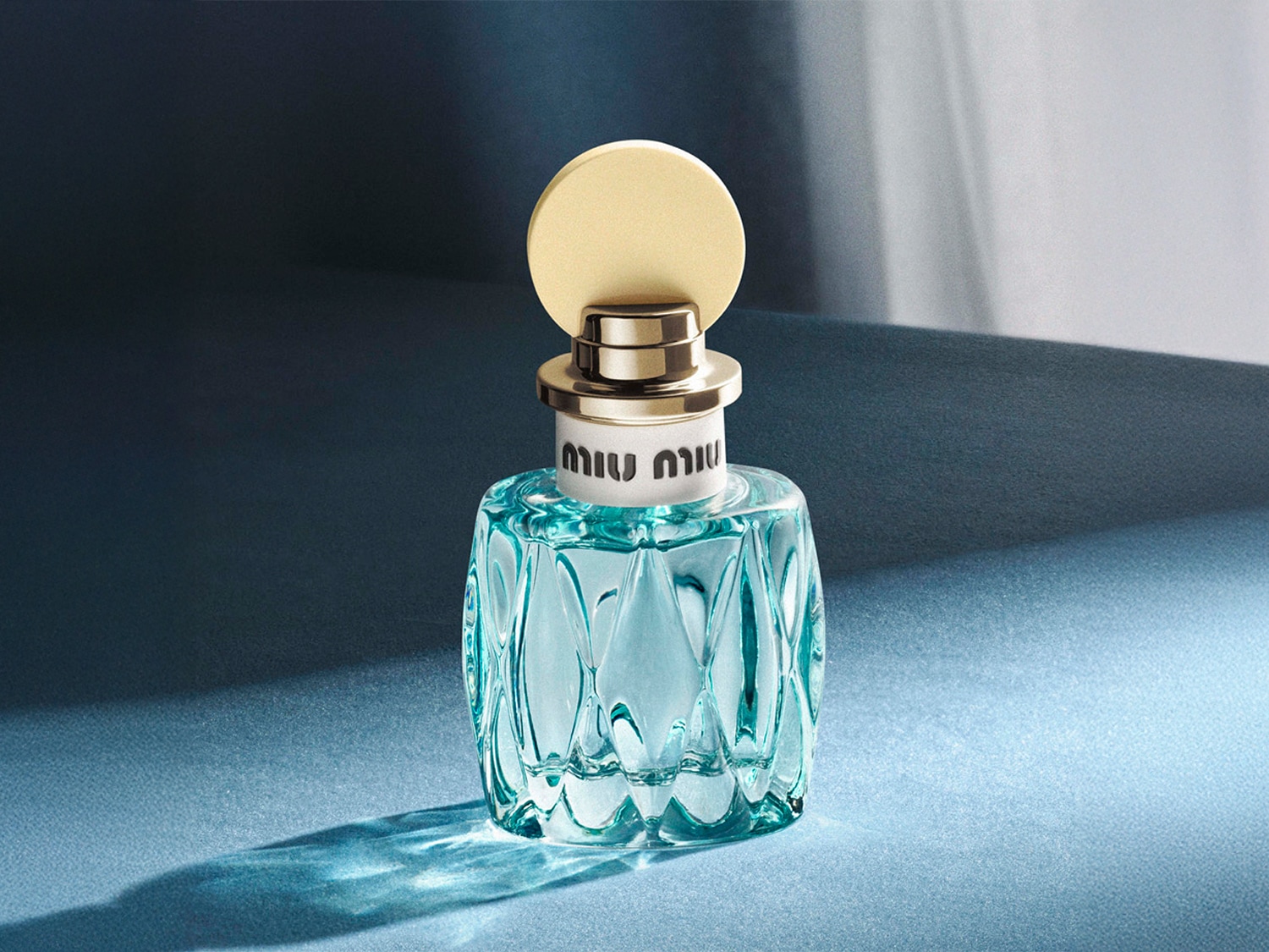 Découvrez le parfum Miu Miu, présenté dans un flacon en verre bleu azur aux détails dorés, évoquant fraîcheur et élégance.