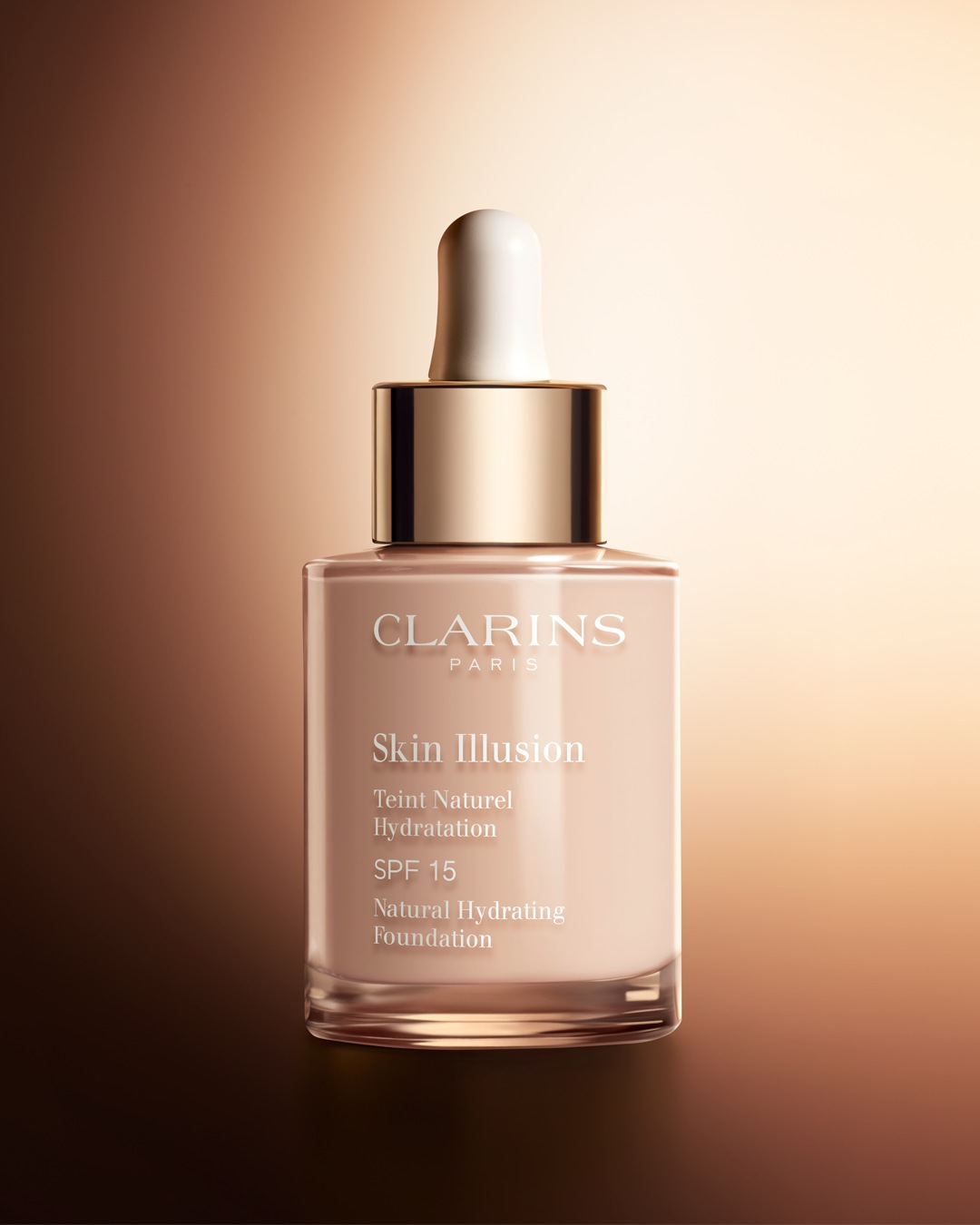 Een fles Clarins Skin Illusion Natural Hydrating Foundation SPF 15, met een lichtbeige vloeistof en een gouden dop met een witte applicator.