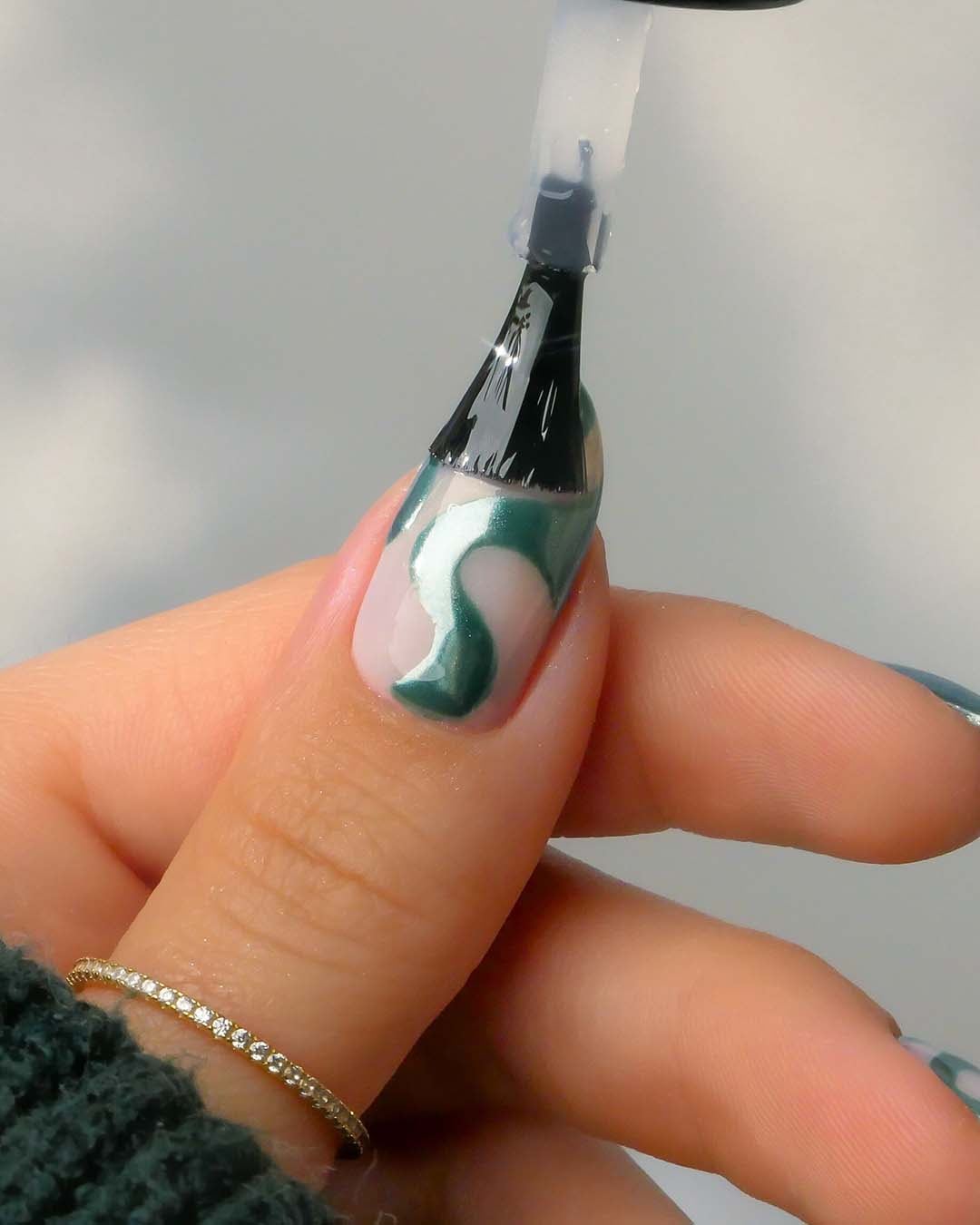 Nahaufnahme einer Hand, die mit einem Pinsel grünen Nagellack in einem geschwungenen Design auf einen Fingernagel aufträgt.