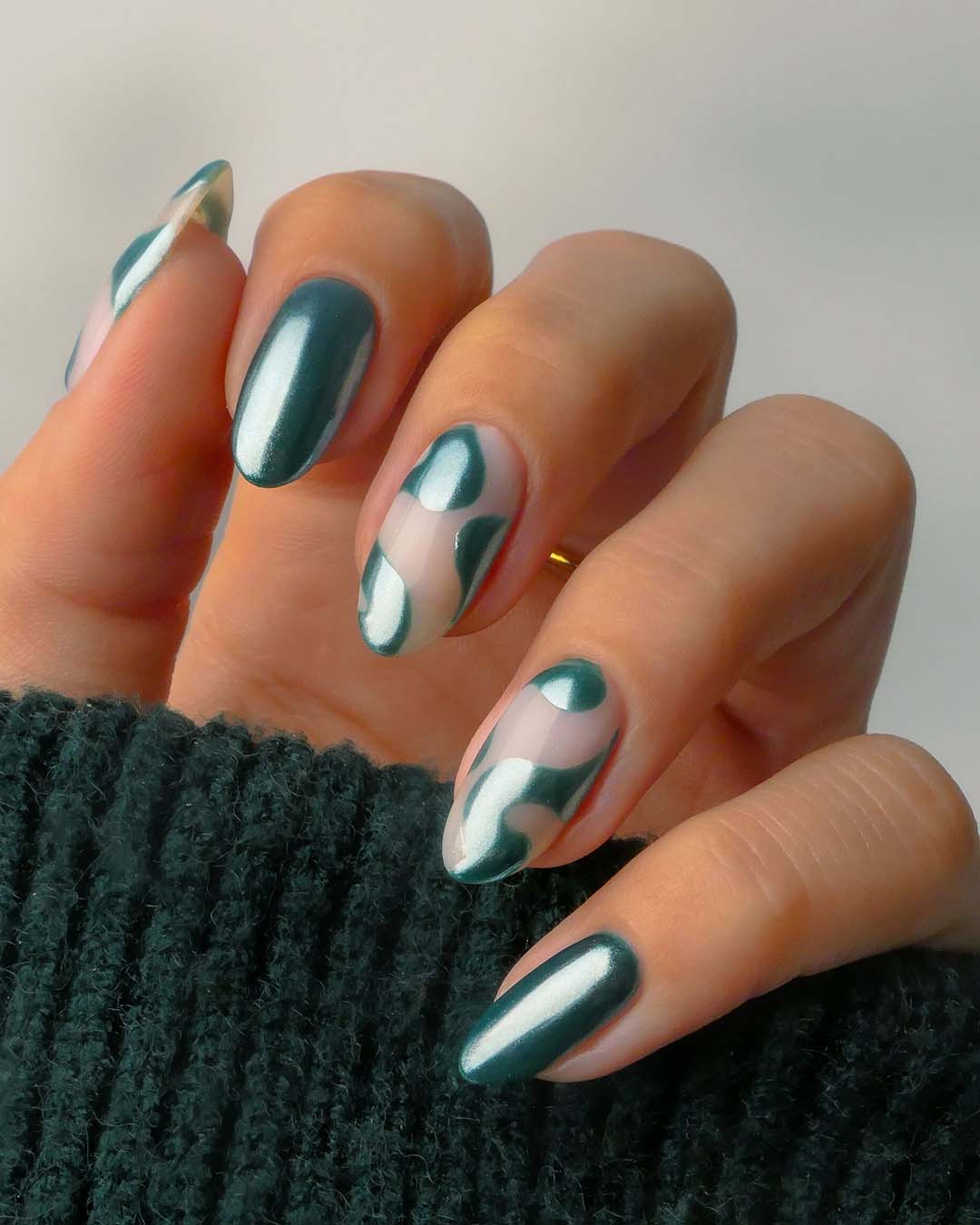 Nahaufnahme einer Hand mit ovalen Nägeln, lackiert in glänzendem Dunkelgrün und abstraktem Design.