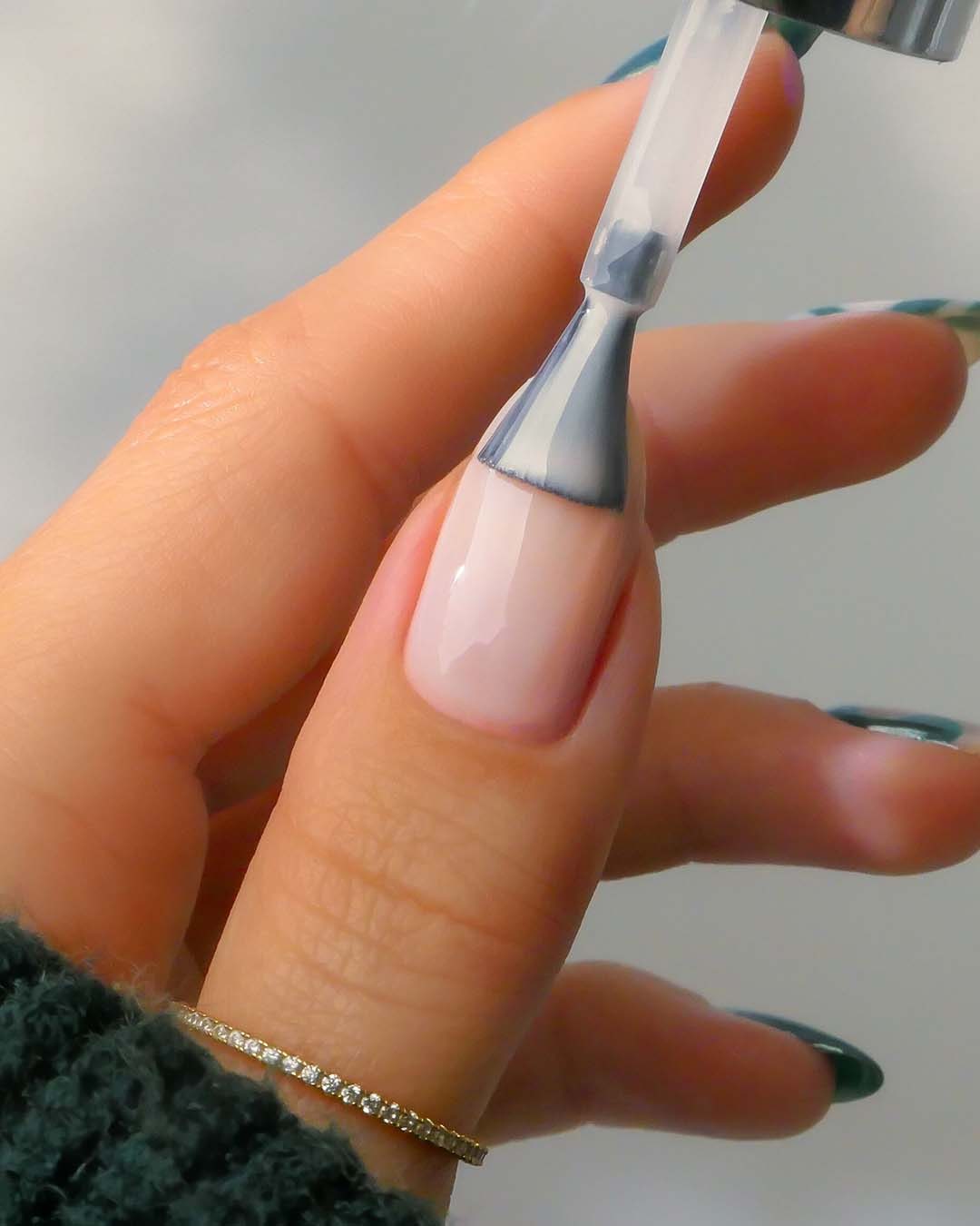 Nahaufnahme einer Hand, die einen hellrosa Nagellack mit einem Pinsel aufträgt, während ein goldener Ring am Finger funkelt.