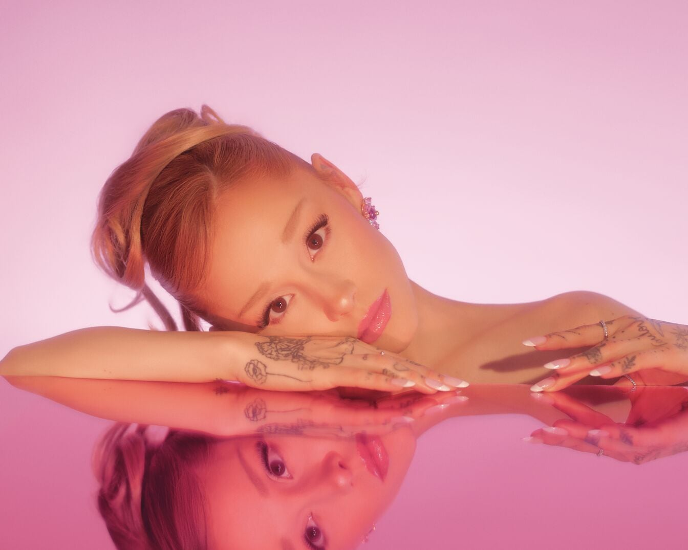 Ariana Grande R.E.M. Cherry Eclipse kollekciójának képe, rózsaszín háttérrel, amely az énekesnő tükörképét mutatja.