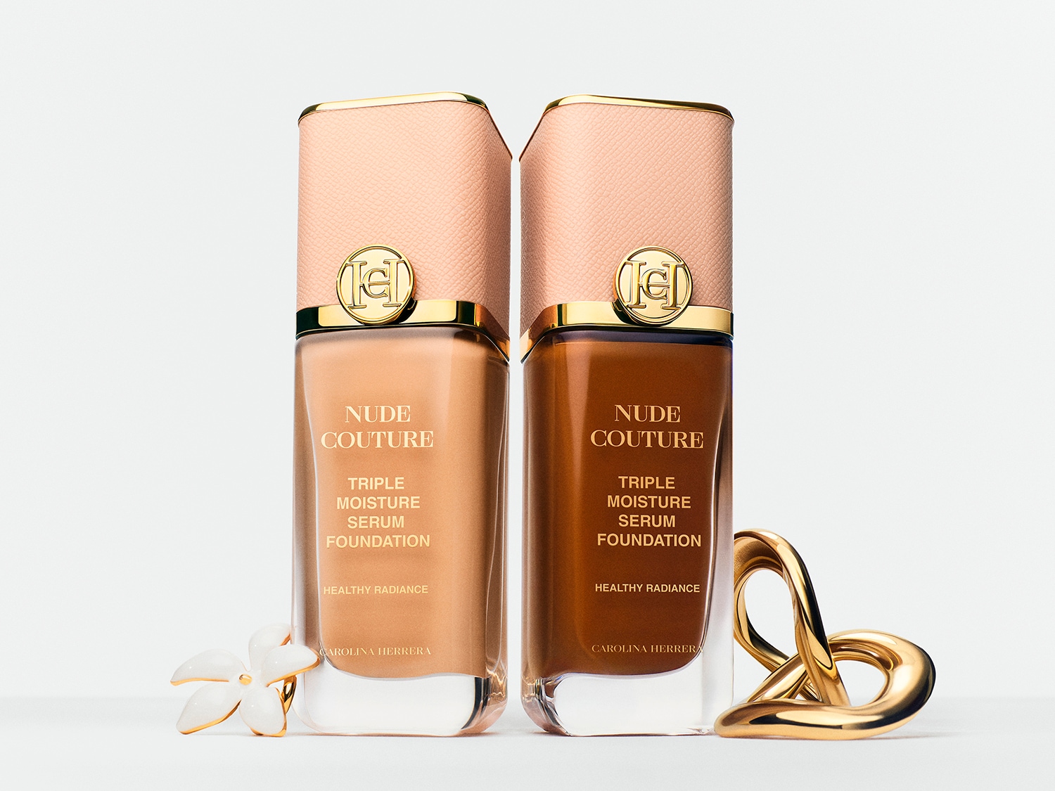 Nahaufnahme von Carolina Herrera Make-up-Anhängern in Rosa-, Rot- und Lilatönen mit goldenen Akzenten, die auf einem Hintergrund aus schimmerndem Lidschatten in Rosa-, Rot- und Grautönen liegen.