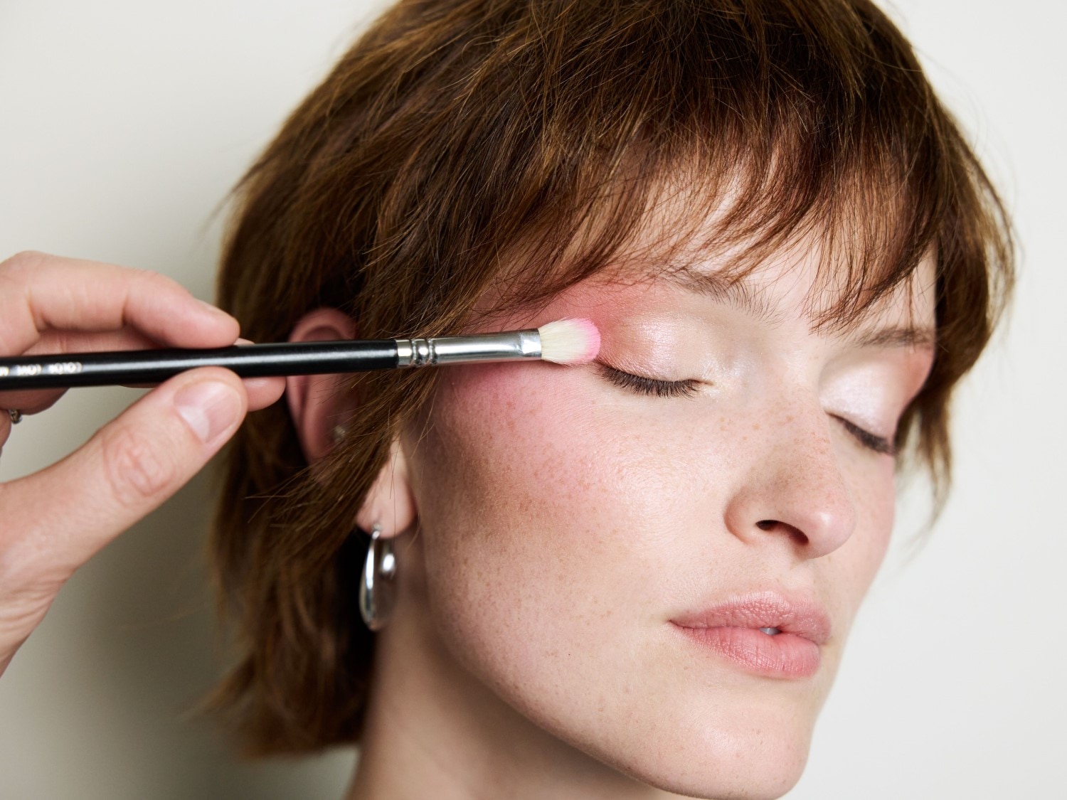 Ein Make-up-Artist trägt mit einem Pinsel rosa Lidschatten auf das Augenlid eines Models auf, um einen sanften und strahlenden Look zu erzielen.