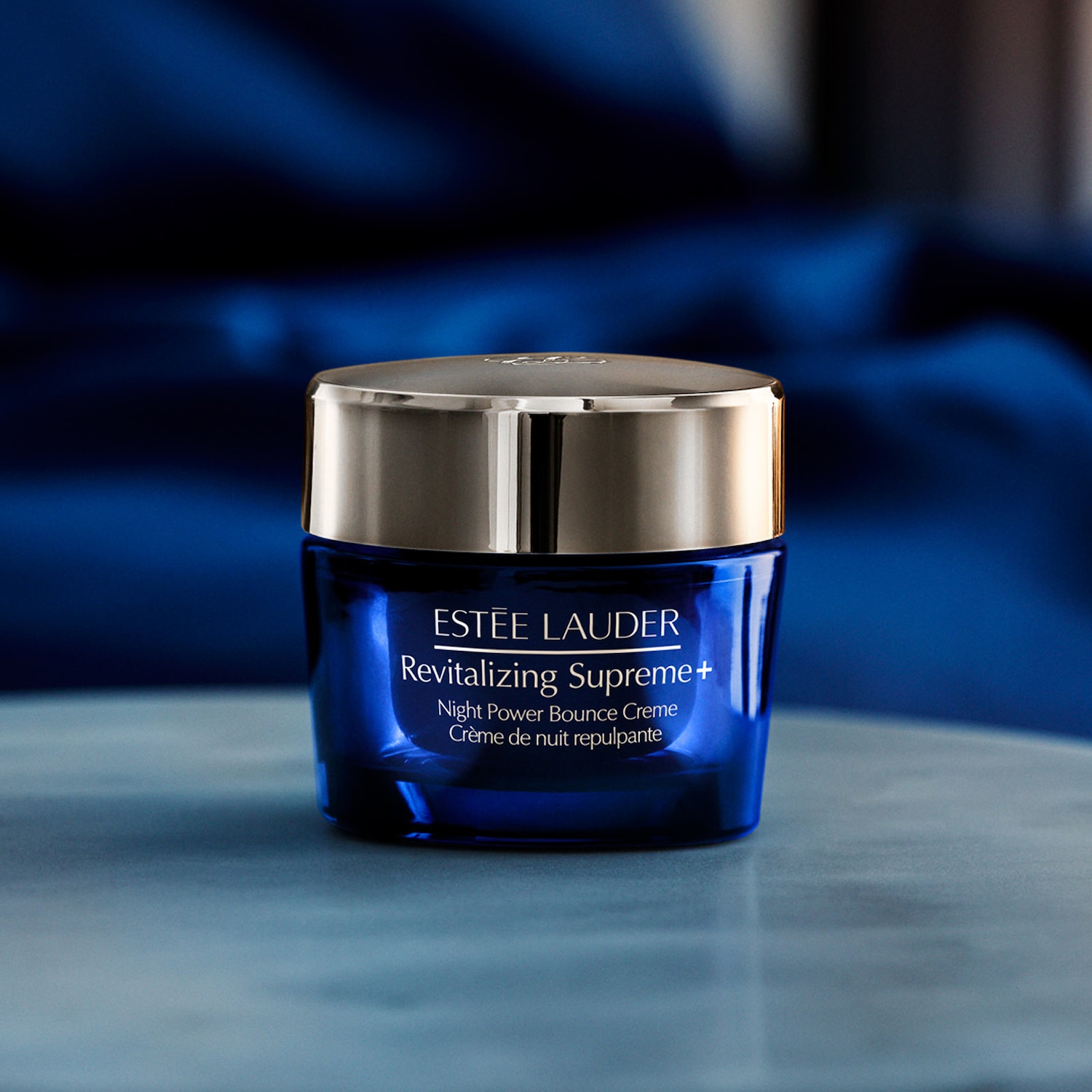 Nahaufnahme eines Tiegel Estée Lauder Revitalizing Supreme+ Night Power Bounce Creme, dessen Verpackung in einem dunklen Blauton gehalten ist und einen goldenen Deckel besitzt.