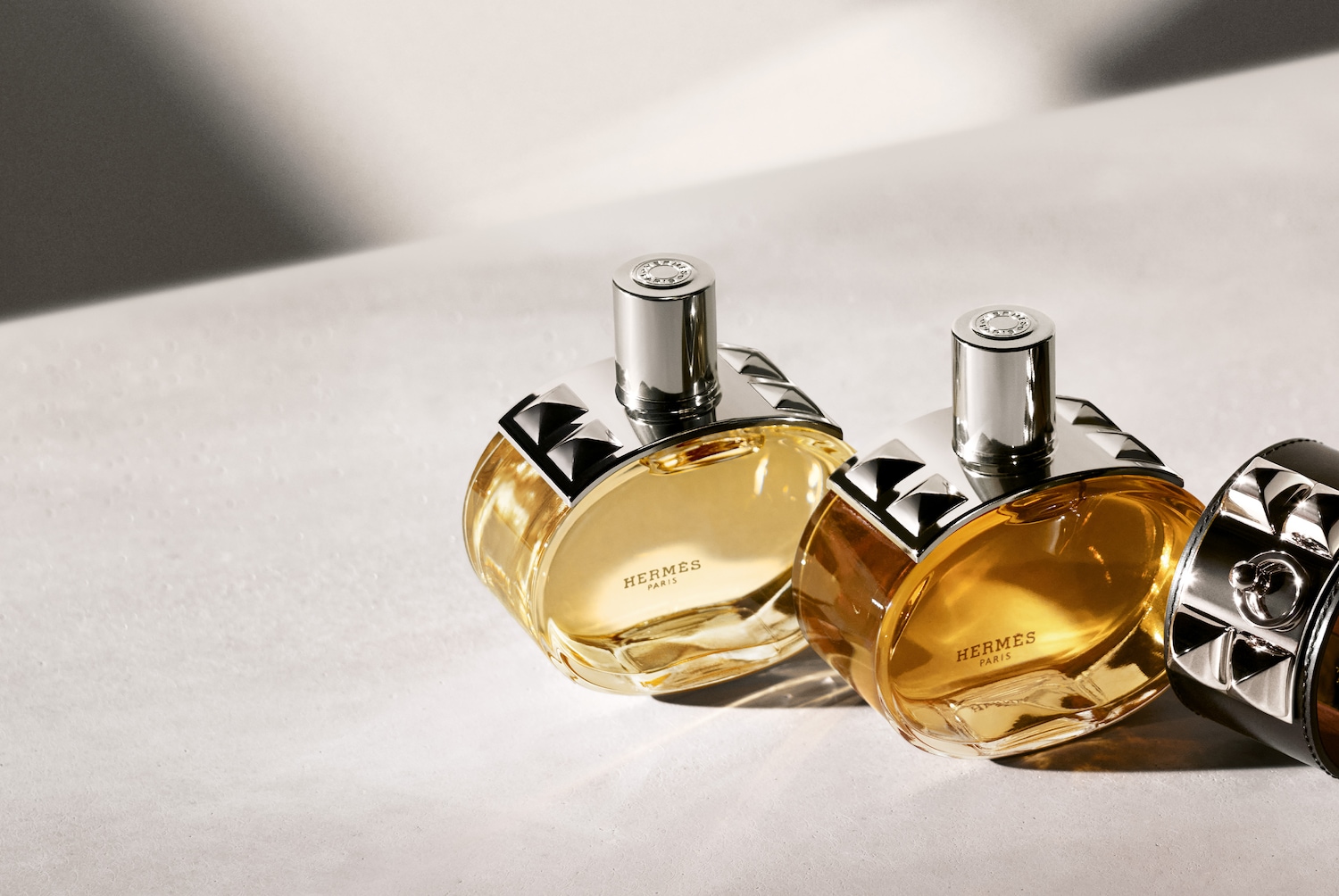 Nahaufnahme von zwei Flakons des Hermès Paris Eau de Toilette mit goldenem Farbton und silbernen Akzenten, die Eleganz und Raffinesse ausstrahlen.