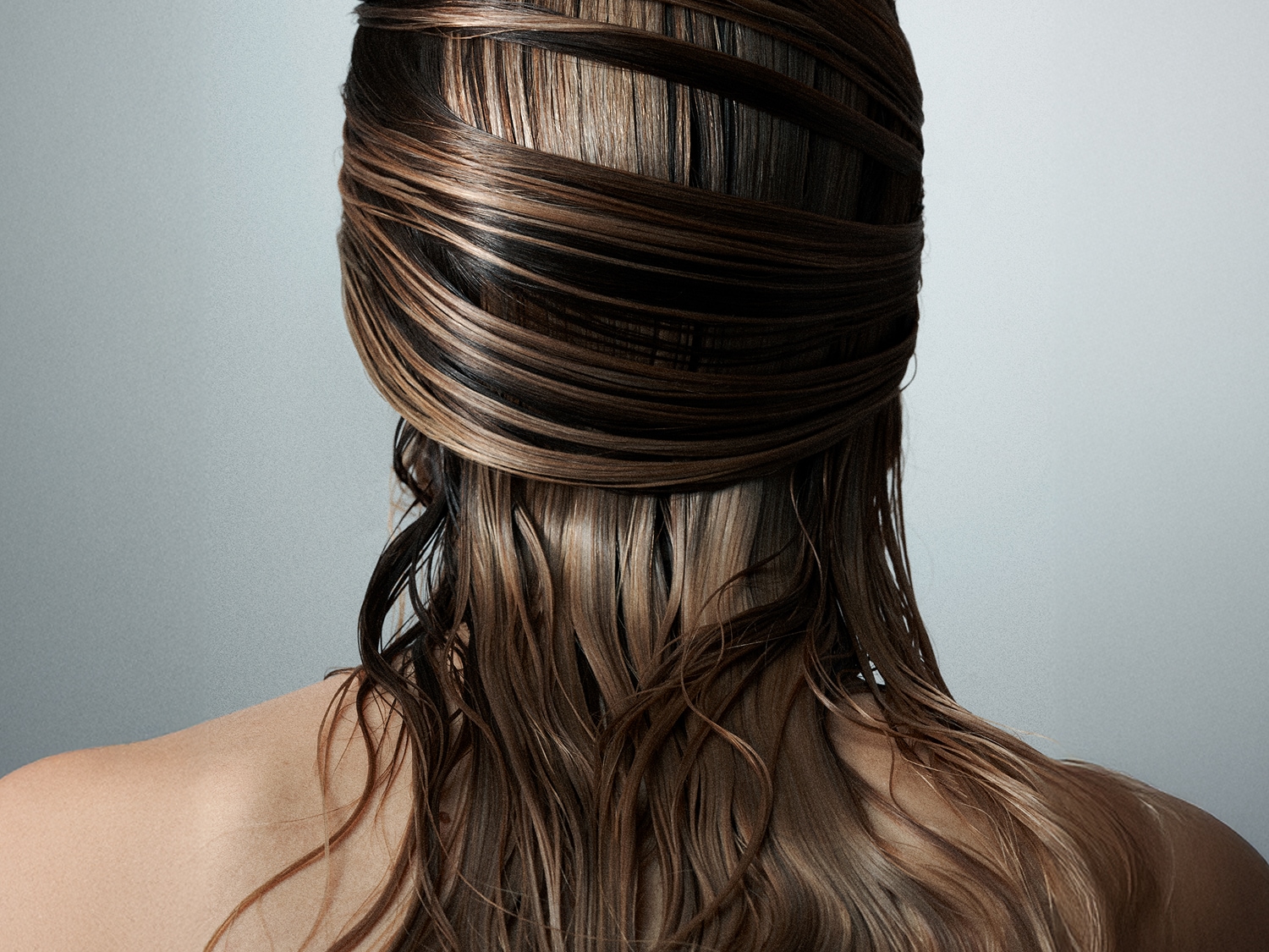 Widok z tyłu kobiety z mokrymi, brązowymi włosami, które są owinięte wokół jej głowy, tworząc efektowną fryzurę.