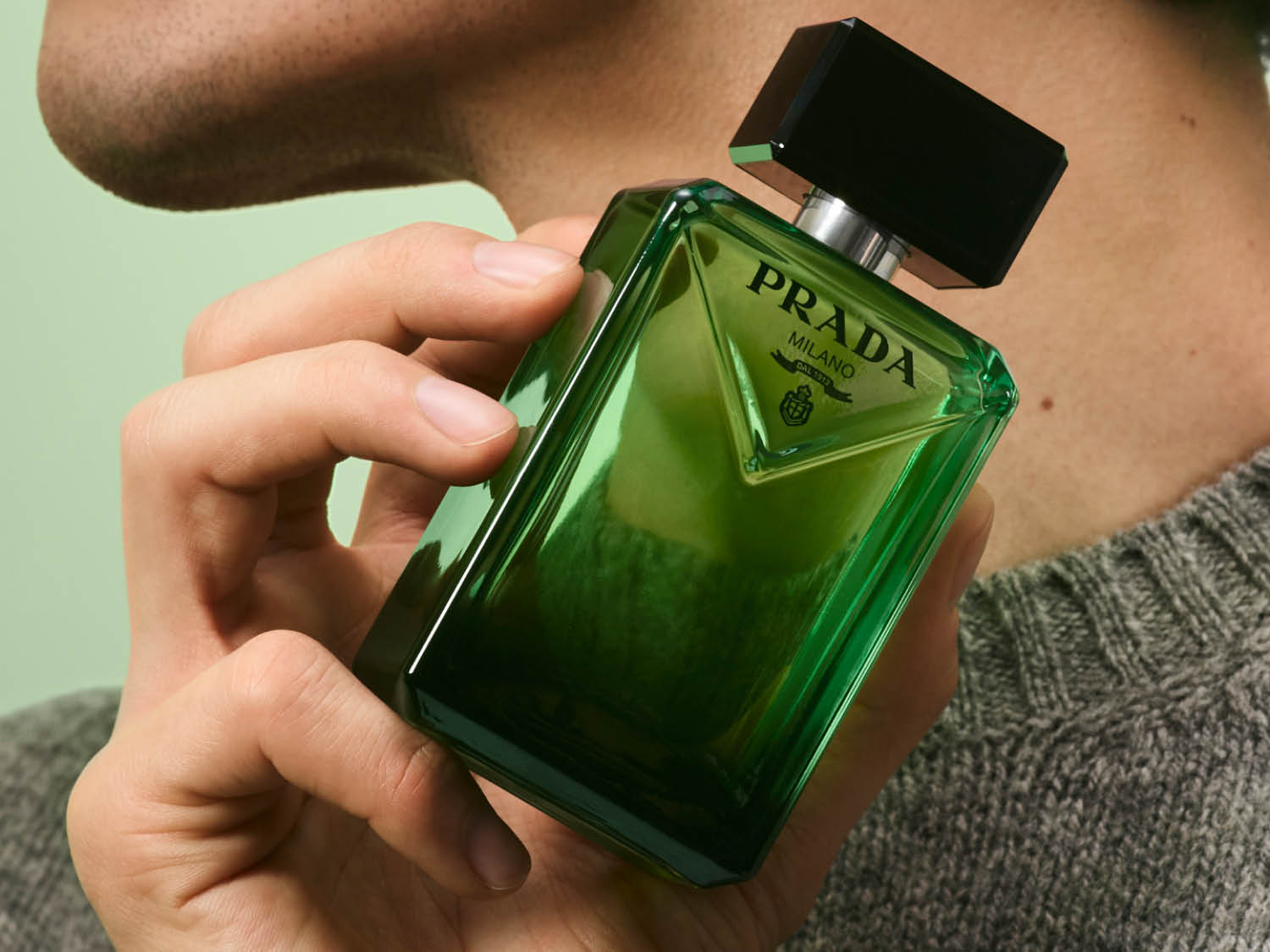 Un homme tient un flacon de parfum Prada vert émeraude avec un bouchon noir, reflétant l'élégance et le style.