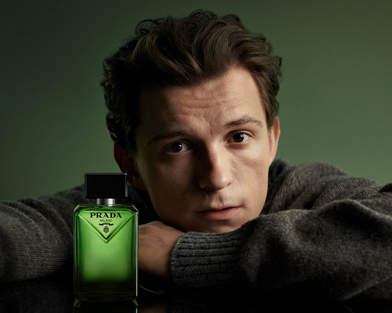Tom Holland pose avec le parfum Prada dans un flacon vert élégant, incarnant le style et le charme de la marque.