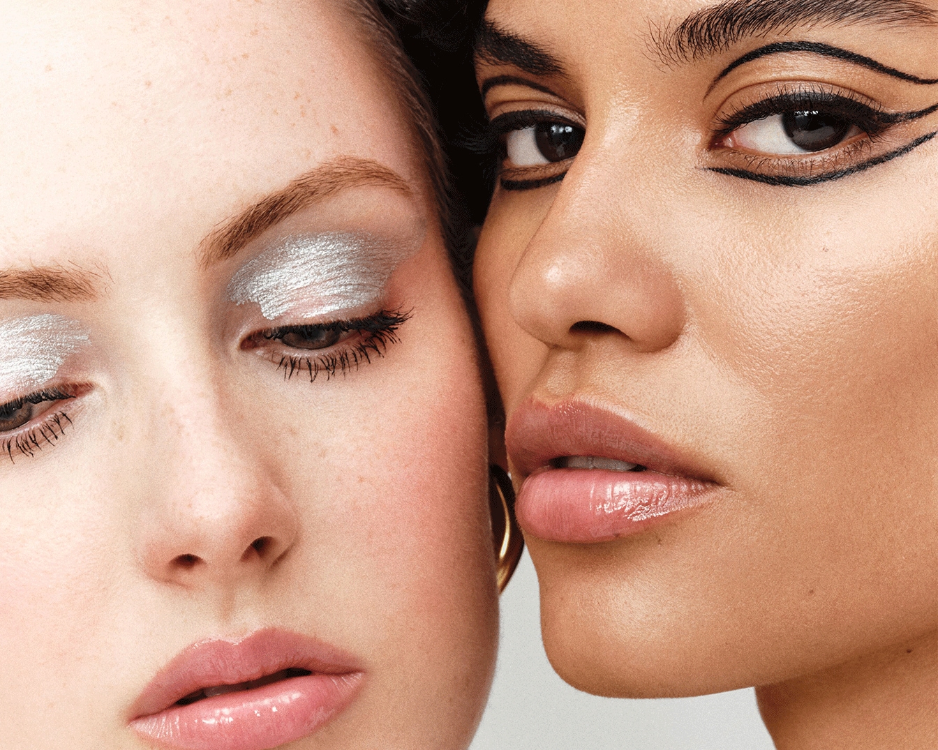 Dviejų moterų veidai iš arti: viena su sidabriniais akių šešėliais, kita – su juodu akių kontūru, pabrėžiančiu akis, ir abi su blizgančiomis lūpomis.