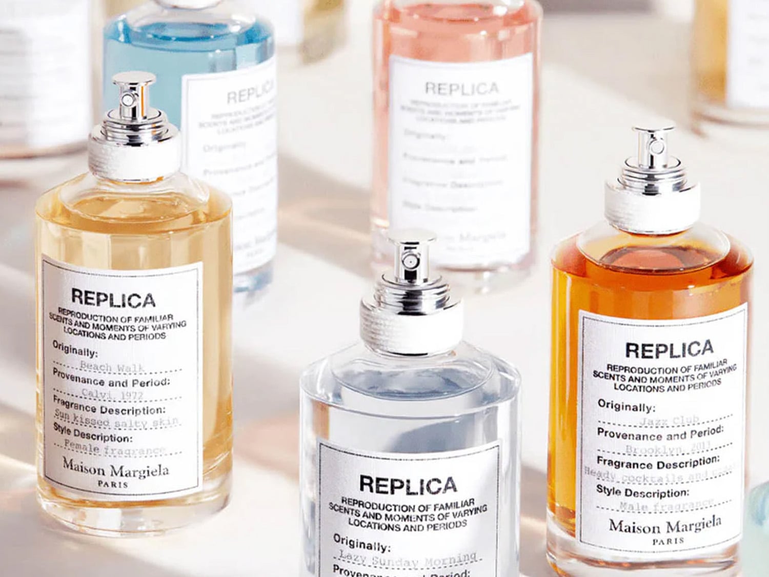 Flakony perfum Maison Margiela Replica w różnych kolorach, od złotego Beach Walk po błękitny i różowy, każdy z etykietą.