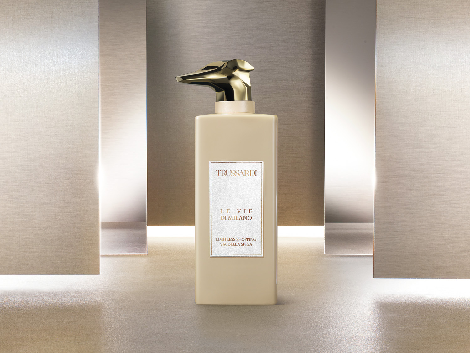 Kremowa butelka Trussardi Le Vie Di Milano z złotą pompką w kształcie głowy psa, elegancko prezentuje się na tle metalowych paneli.