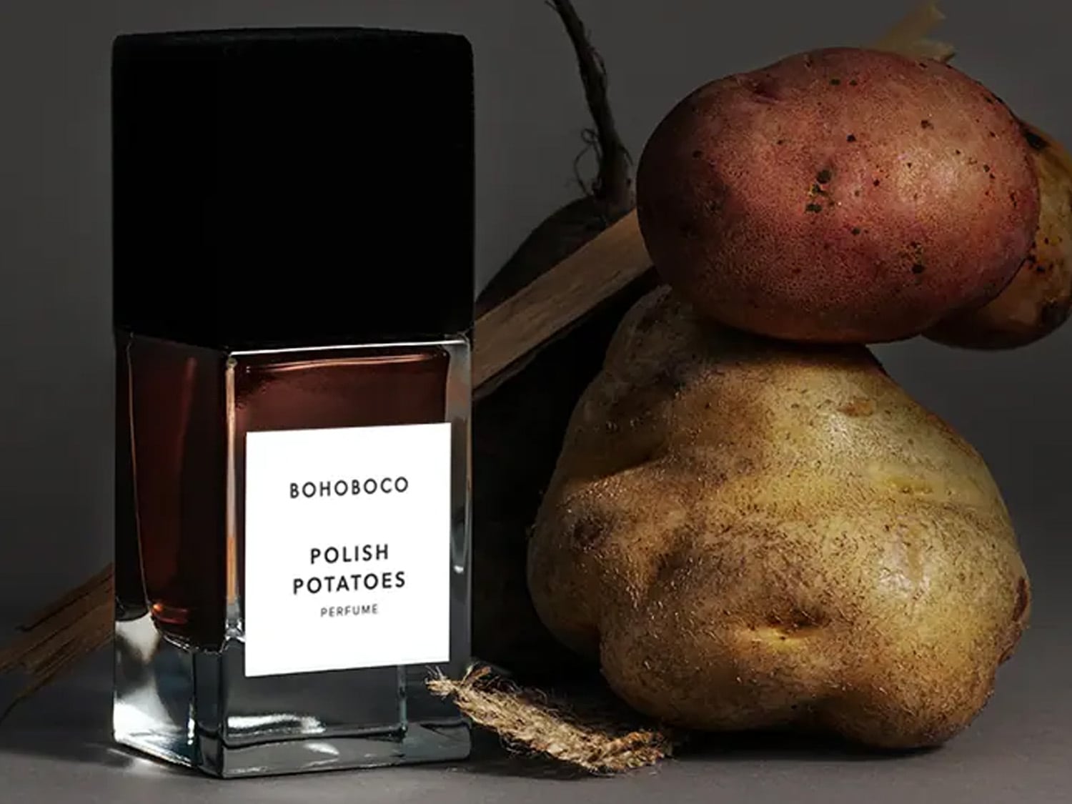 Butelka perfum Bohoboco Polish Potatoes z brązowym płynem i czarną nakrętką stoi obok ziemniaków.