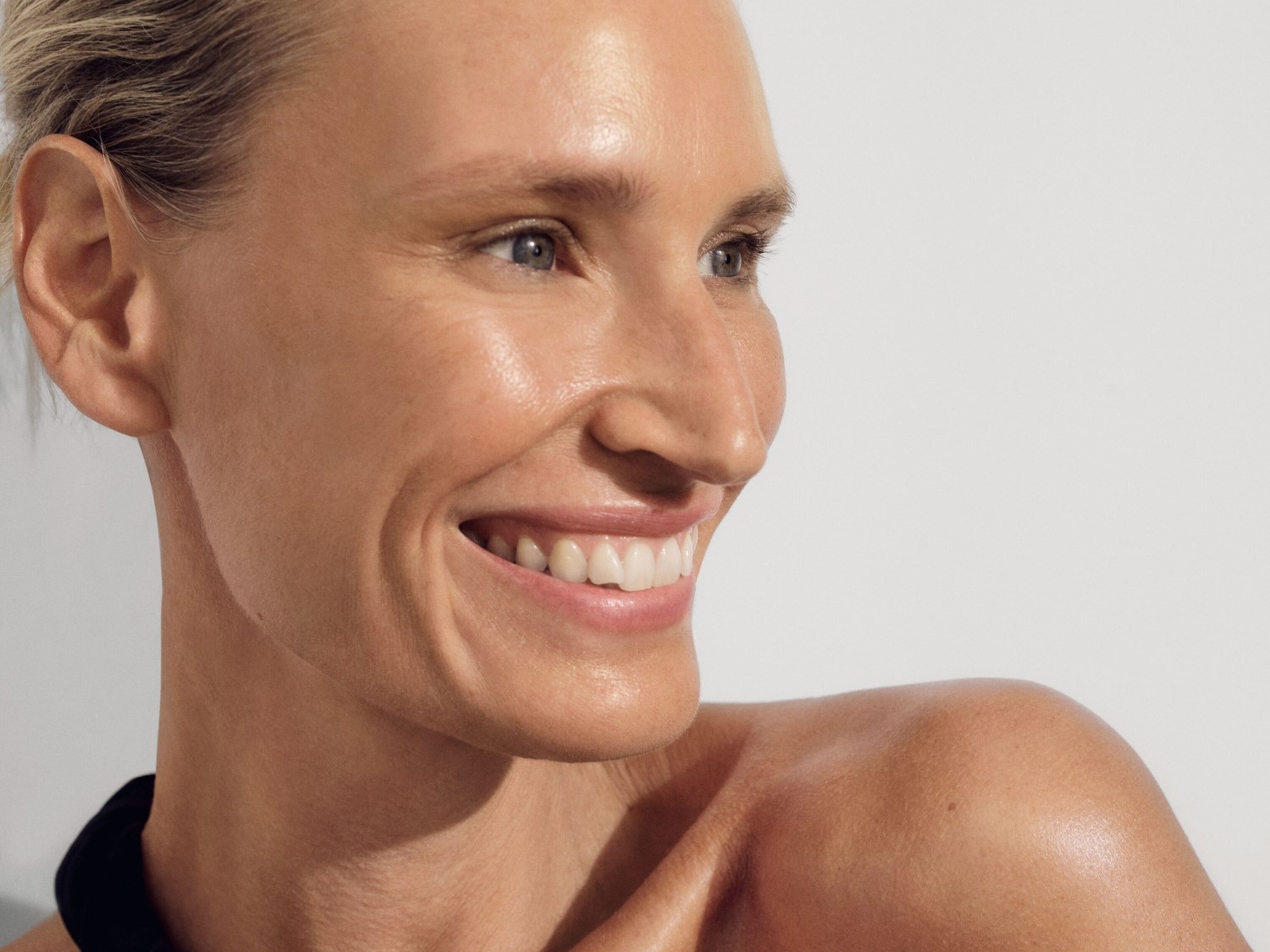 Portrait d'une femme blonde souriante, la peau claire et lumineuse, regardant vers la droite avec une expression joyeuse.