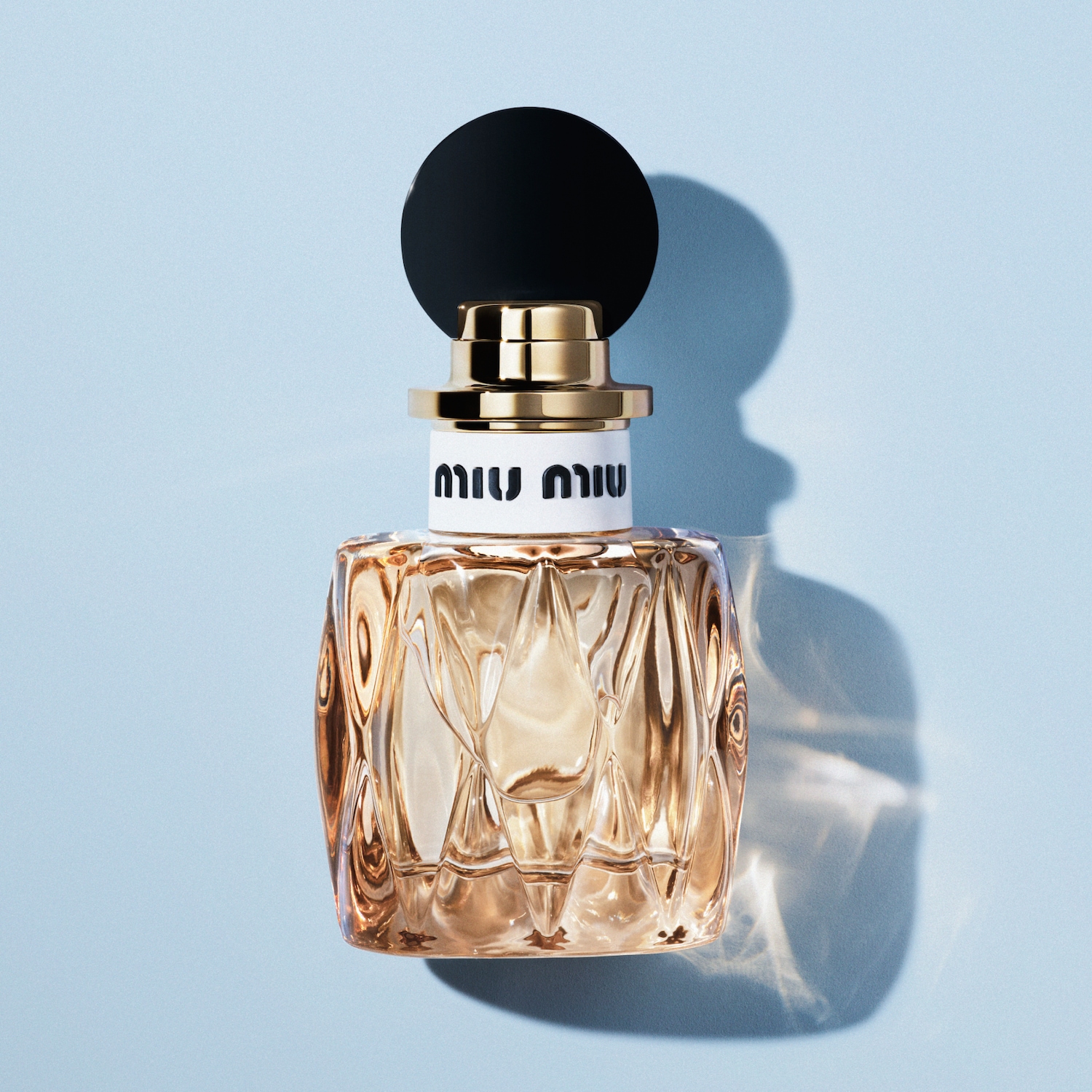 Le parfum Miu Miu, présenté dans un flacon en verre facetté rempli d'un liquide doré, est coiffé d'un bouchon noir et doré élégant.