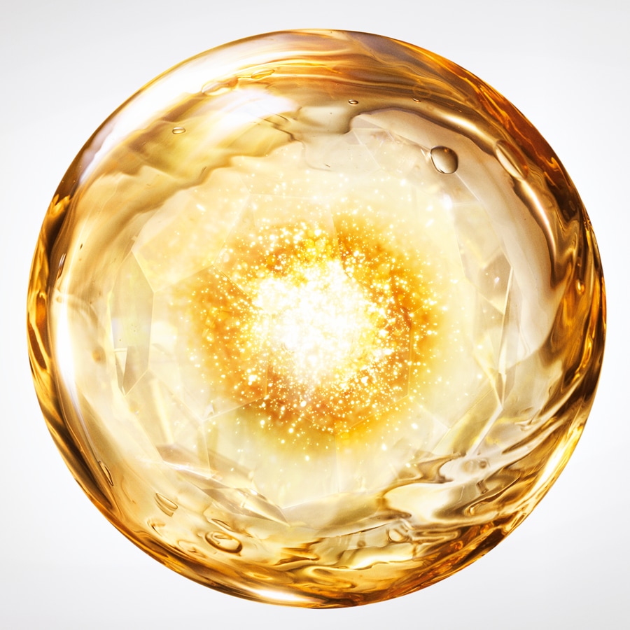 Nahaufnahme einer goldenen Kugel mit einem hellen, sternförmigen Zentrum, das an ein Serum oder Öl für die Hautpflege erinnert.