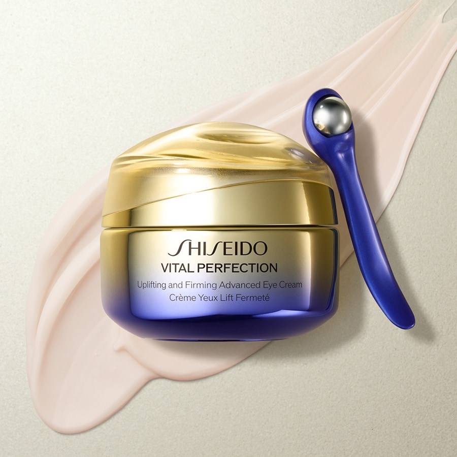 Shiseido Vital Perfection Lifting and Firming Advanced Eye Cream in einem goldenen Tiegel mit blauem Farbverlauf und einem blauen Applikator.