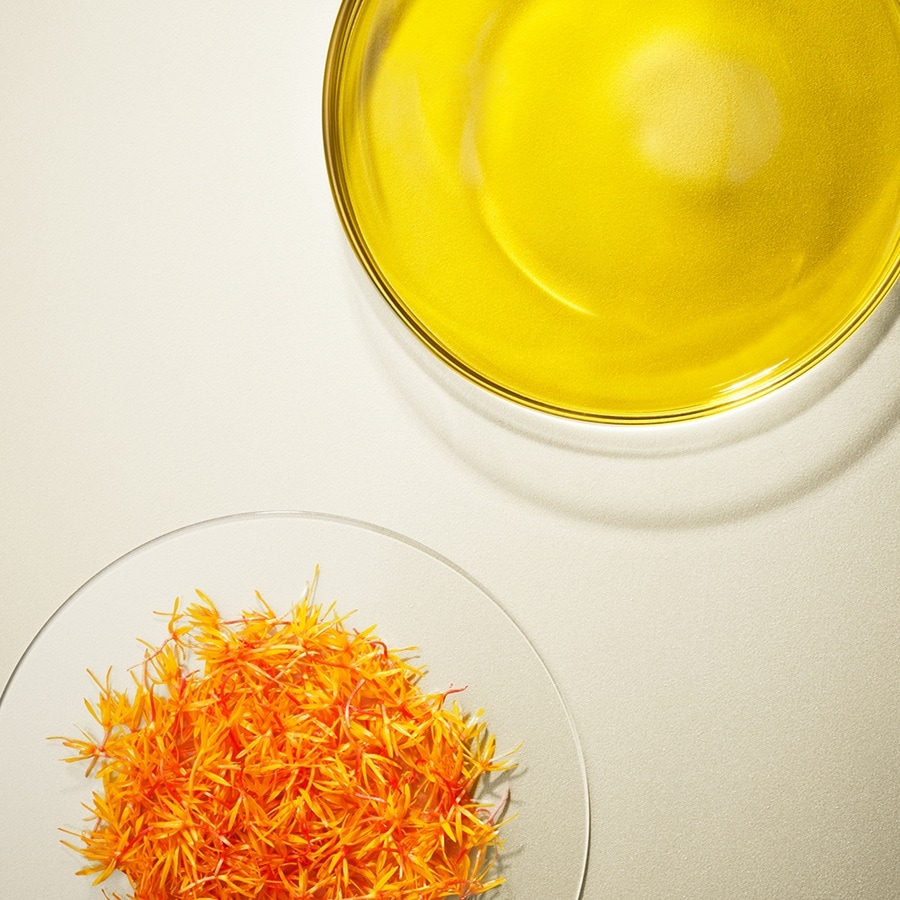 Draufsicht auf eine gelbe Flüssigkeit in einer Glasschale und orangefarbene Blütenblätter in einer anderen Glasschale.