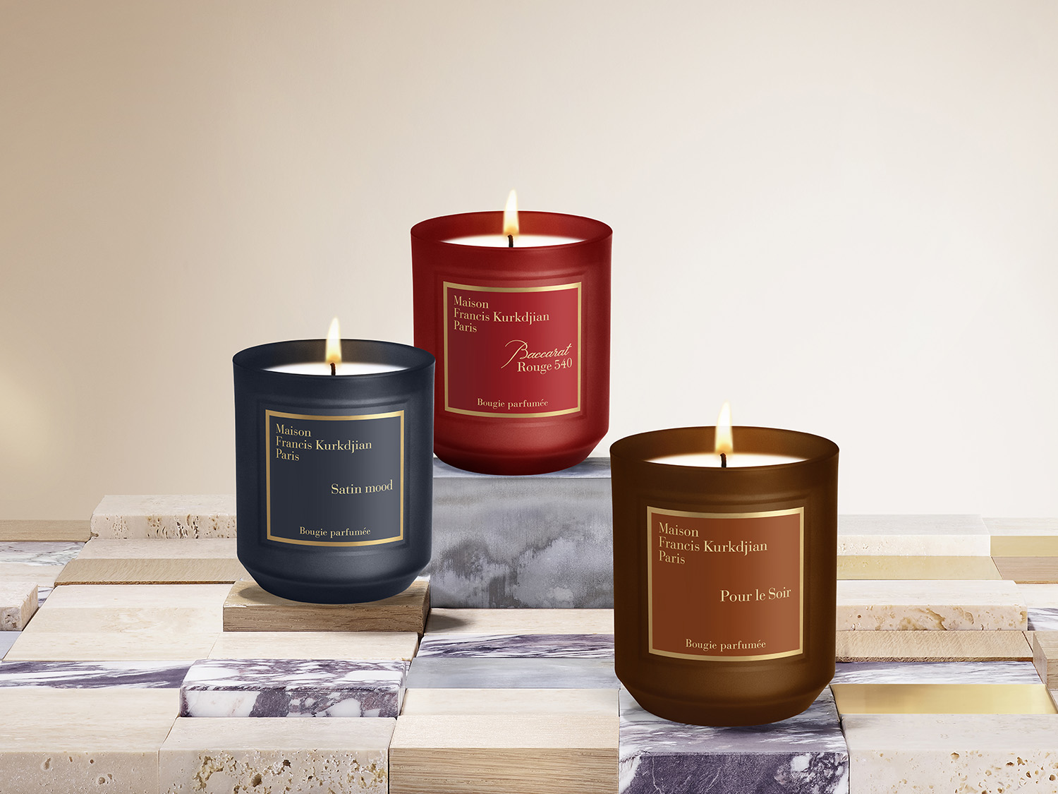 Drei Duftkerzen von Maison Francis Kurkdjian Paris stehen auf einem Mosaiktisch: Satin Mood in einem dunkelblauen Glas, Baccarat Rouge 540 in einem roten Glas und Pour le Soir in einem braunen Glas.
