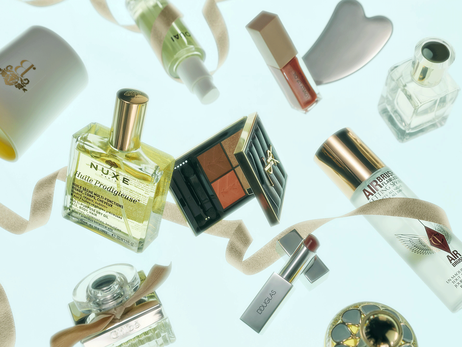 Eine Sammlung von Schönheitsprodukten, darunter Nuxe Huile Prodigieuse Öl, YSL-Lidschattenpalette und Douglas-Lippenstift, die ein luxuriöses Schönheitserlebnis versprechen.