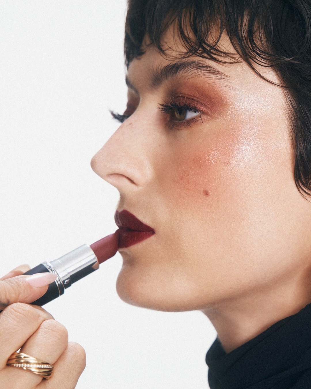 A nő bordó rúzst visz fel, a rúzs ezüst és fekete csomagolásban van, a sminkje pedig bronzos árnyalatú.